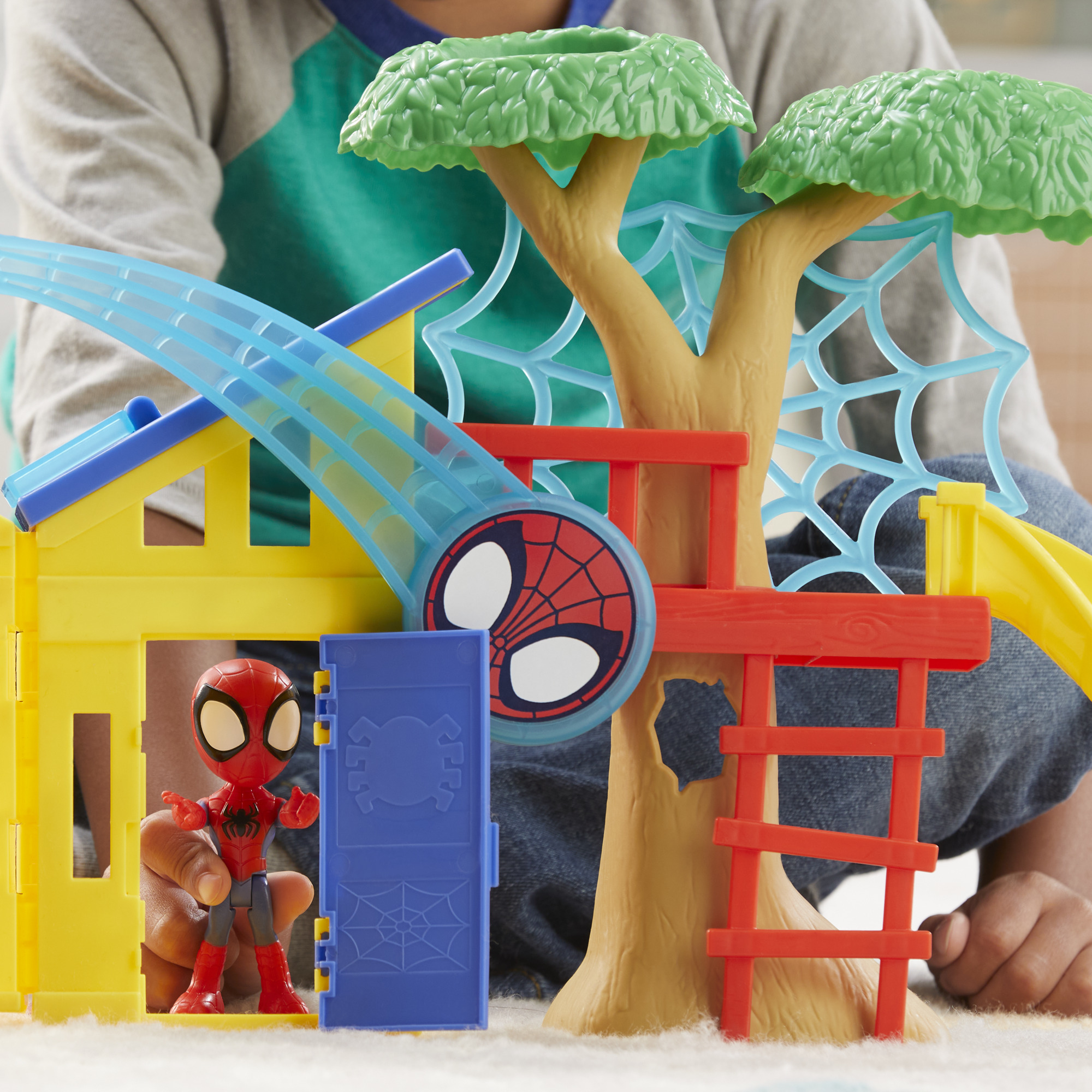 Un bambino gioca con un set di gioco di Spider-Man. È dotato di una casa sull'albero, uno scivolo e una figura di Spider-Man.