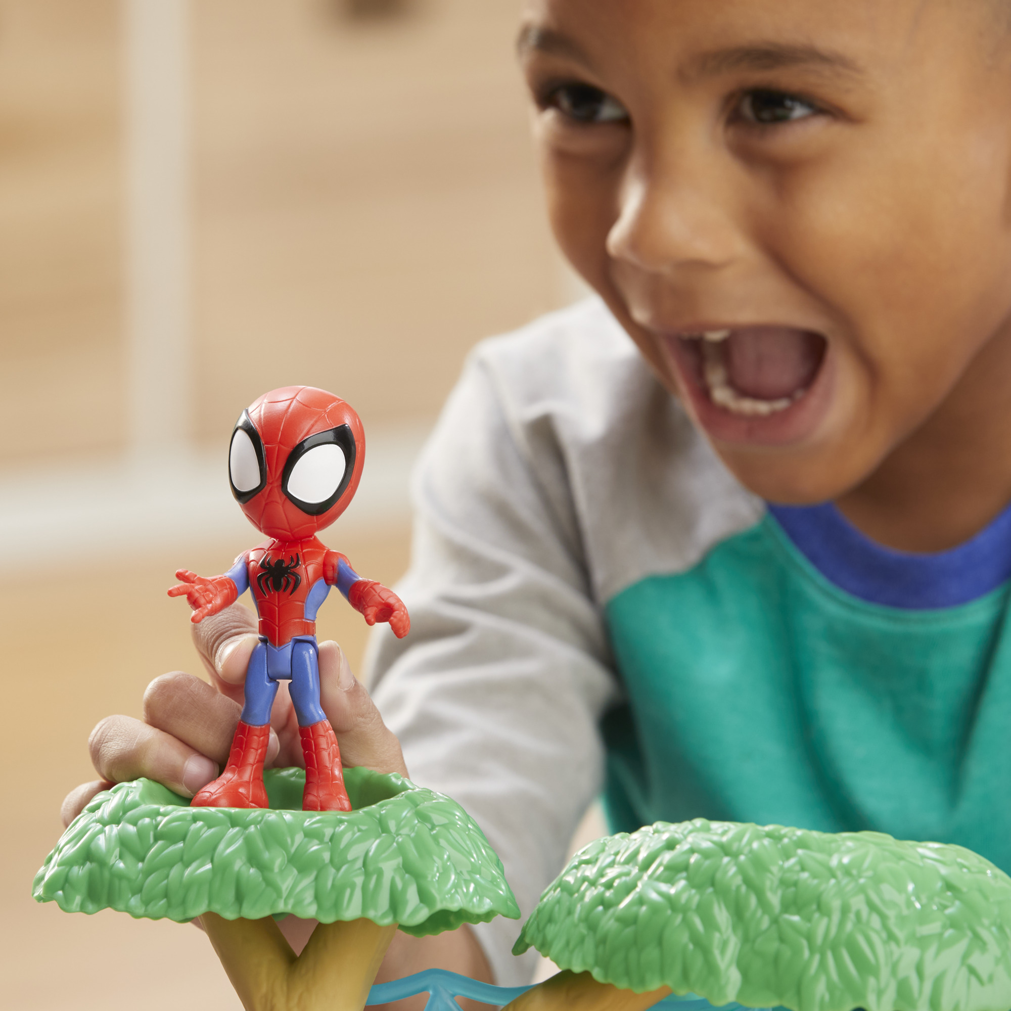 Un ragazzo tiene in mano un giocattolo di Spider-Man. Il giocattolo è rosso, blu e nero. Il ragazzo sorride e ha la bocca aperta.