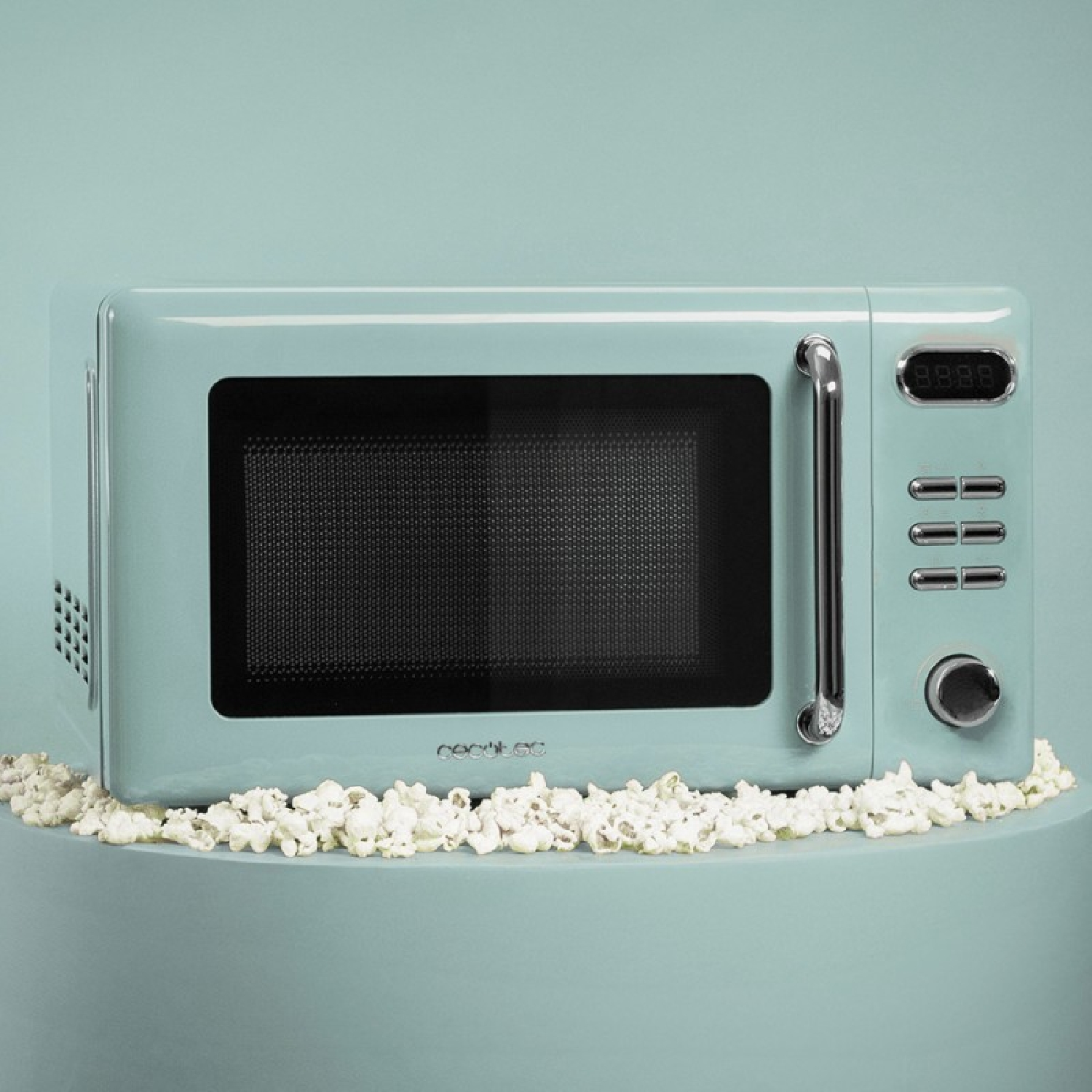 Miętowozielona kuchenka mikrofalowa z popcornem wokół. Kuchenka ma uchwyt i wyświetlacz cyfrowy. Tło jest również miętowo-zielone.