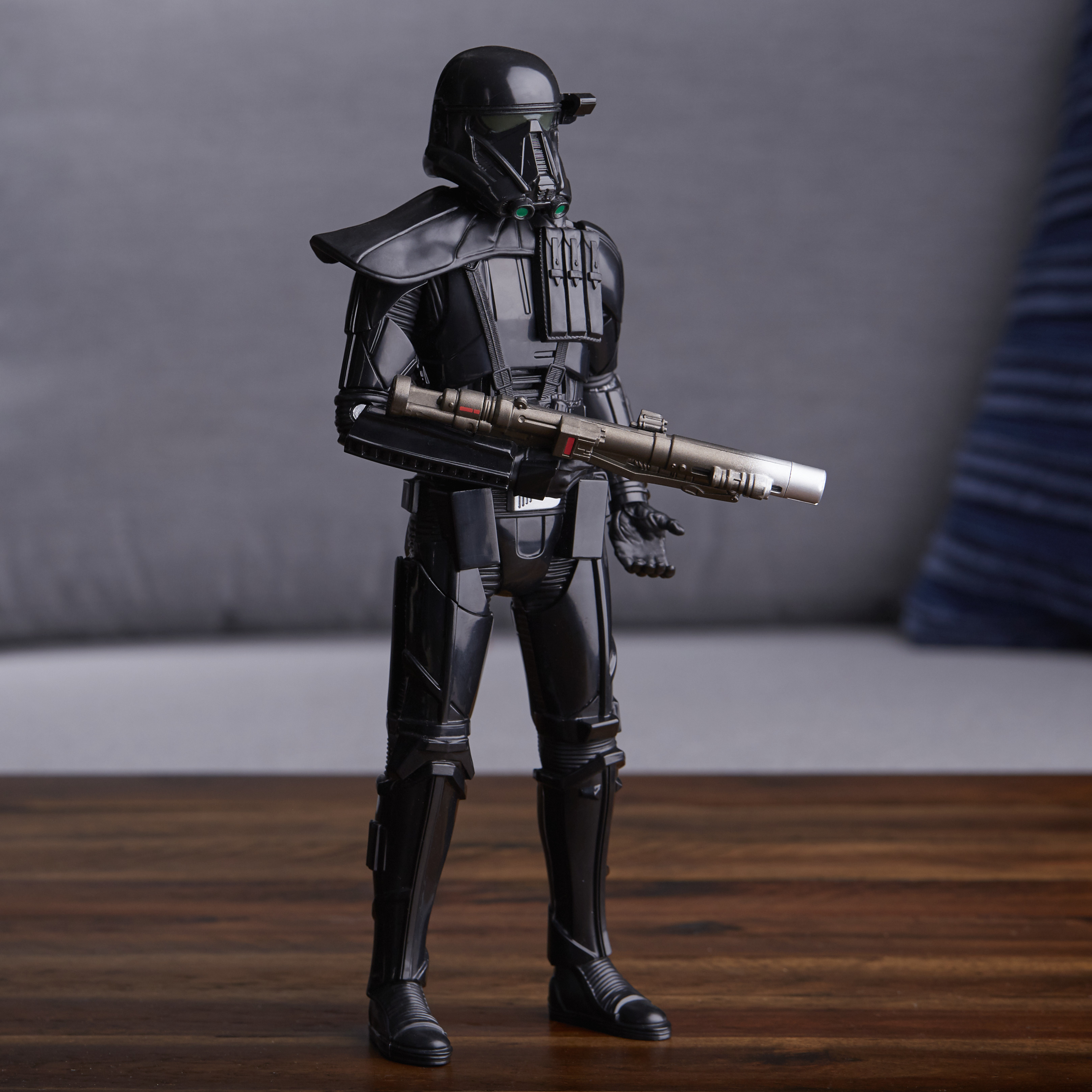 Action figure Death Trooper nera su legno, con blaster. Sfondo grigio e divano.