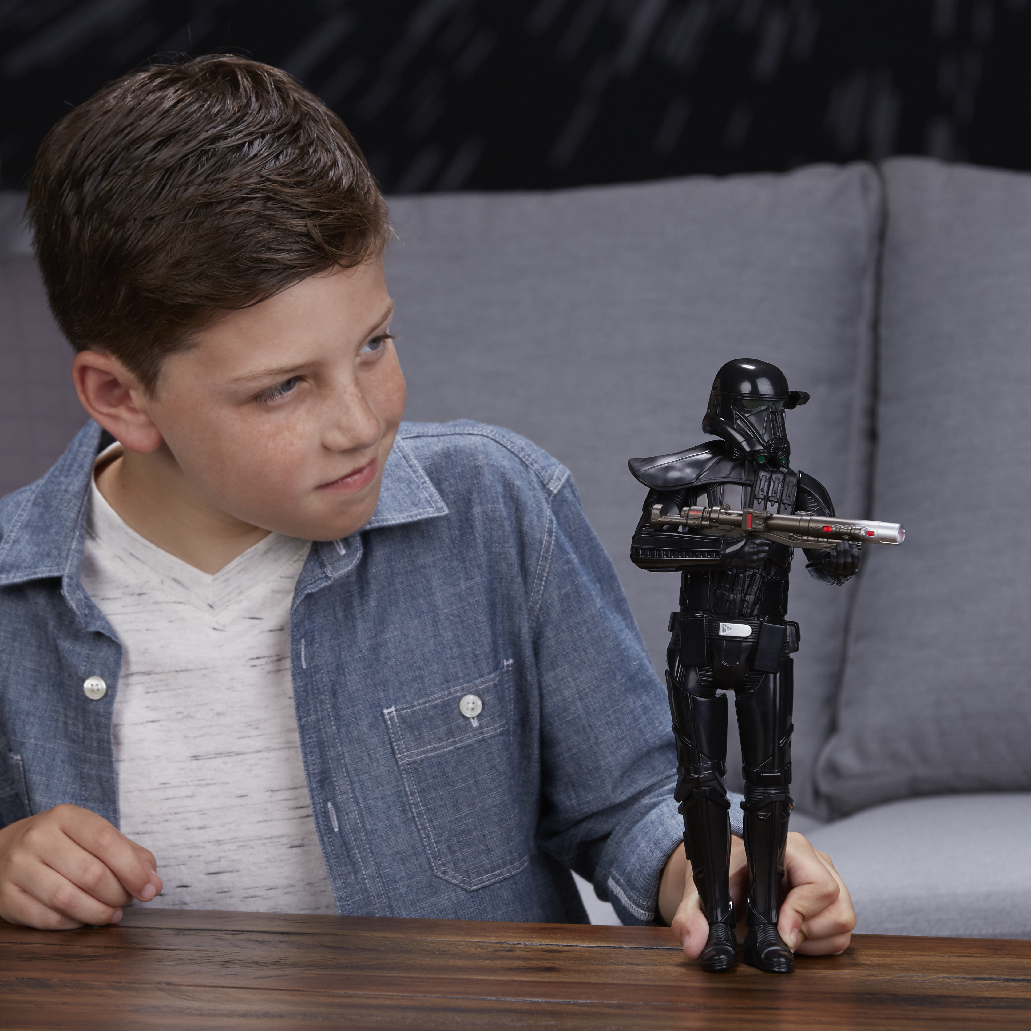 Un ragazzo guarda una figura giocattolo nera di un personaggio di Star Wars, con una pistola, su un tavolo di legno.