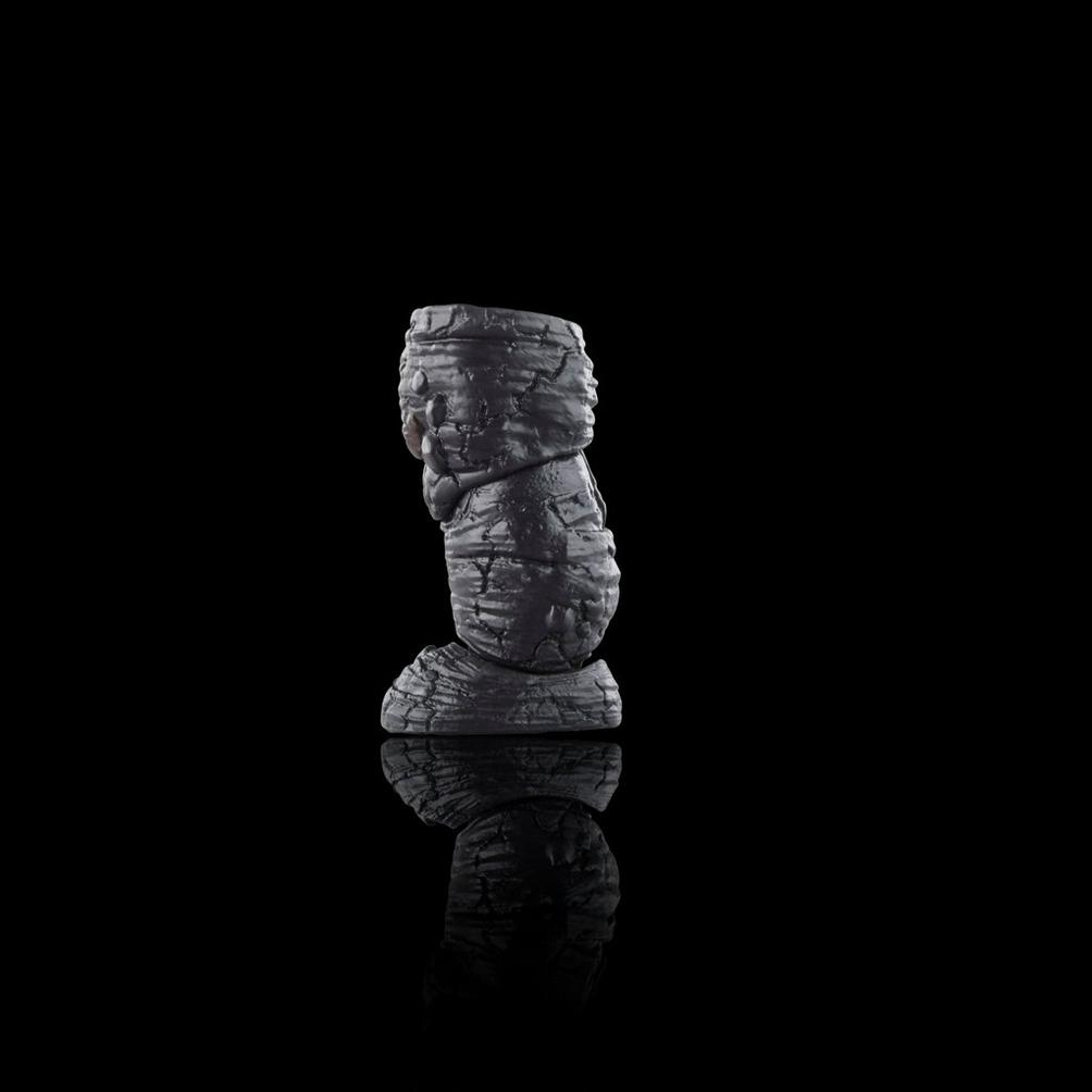 Ciemna, teksturowana rzeźba przypominająca ułożone skały odbija się na czarnej powierzchni. Tło jest całkowicie czarne.