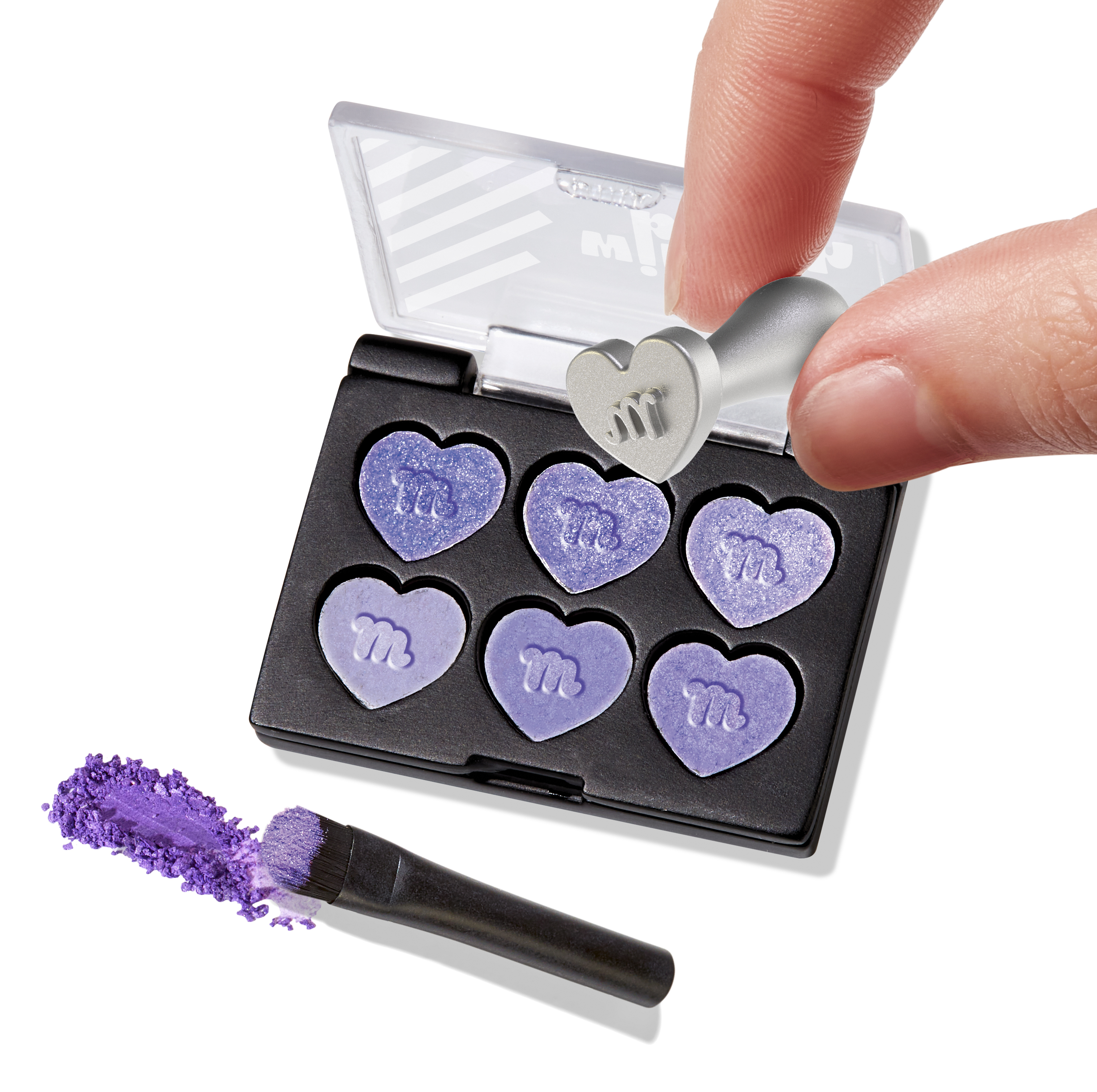 Ręka trzyma stempel w kształcie serca nad paletą cieni do powiek. Fioletowy cień do powiek w kształcie serca. W pobliżu pędzel i puder.