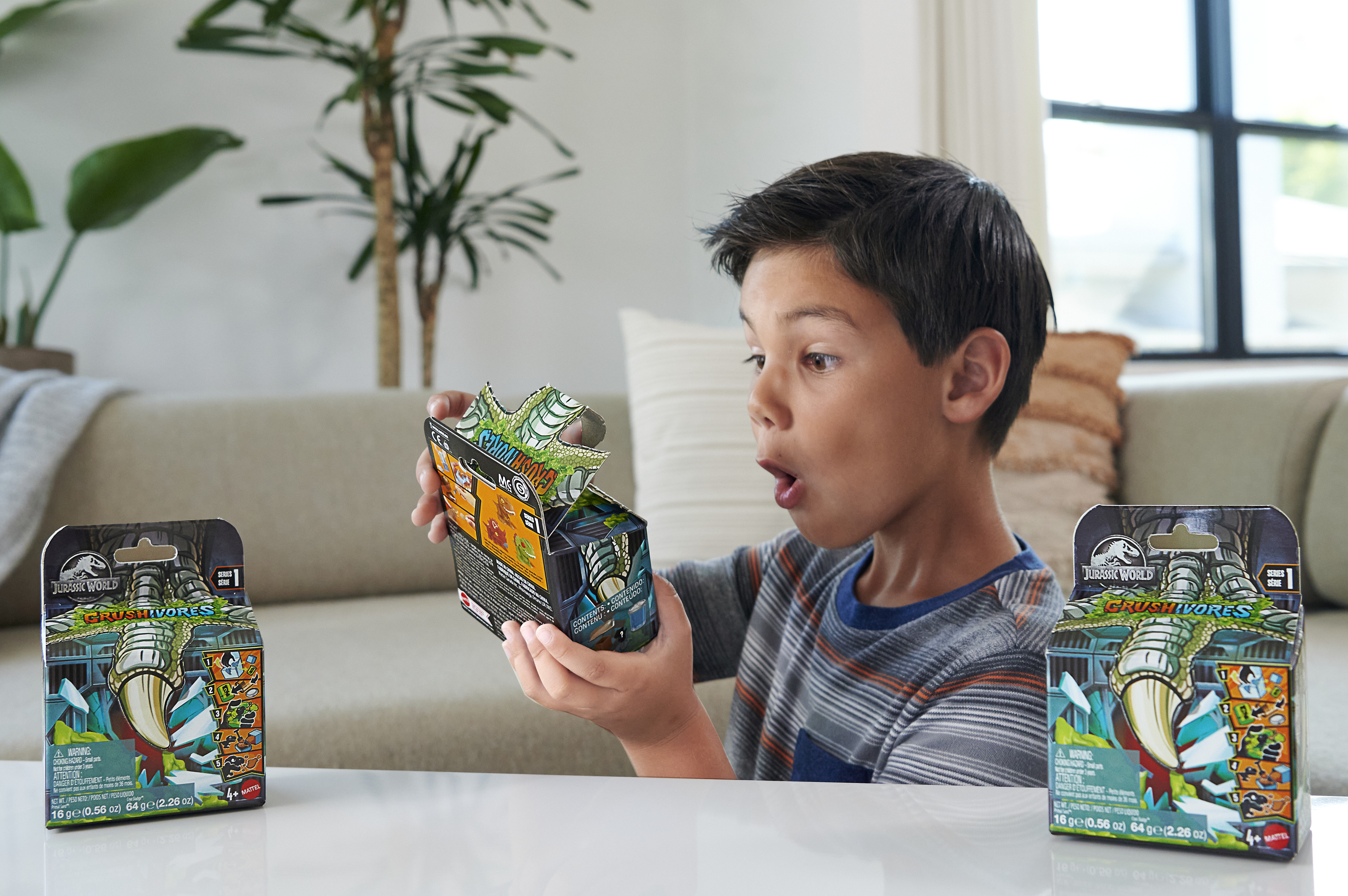 Un niño abre una caja de juguetes de Jurassic World, luciendo sorprendido. Hay dos cajas en la mesa.