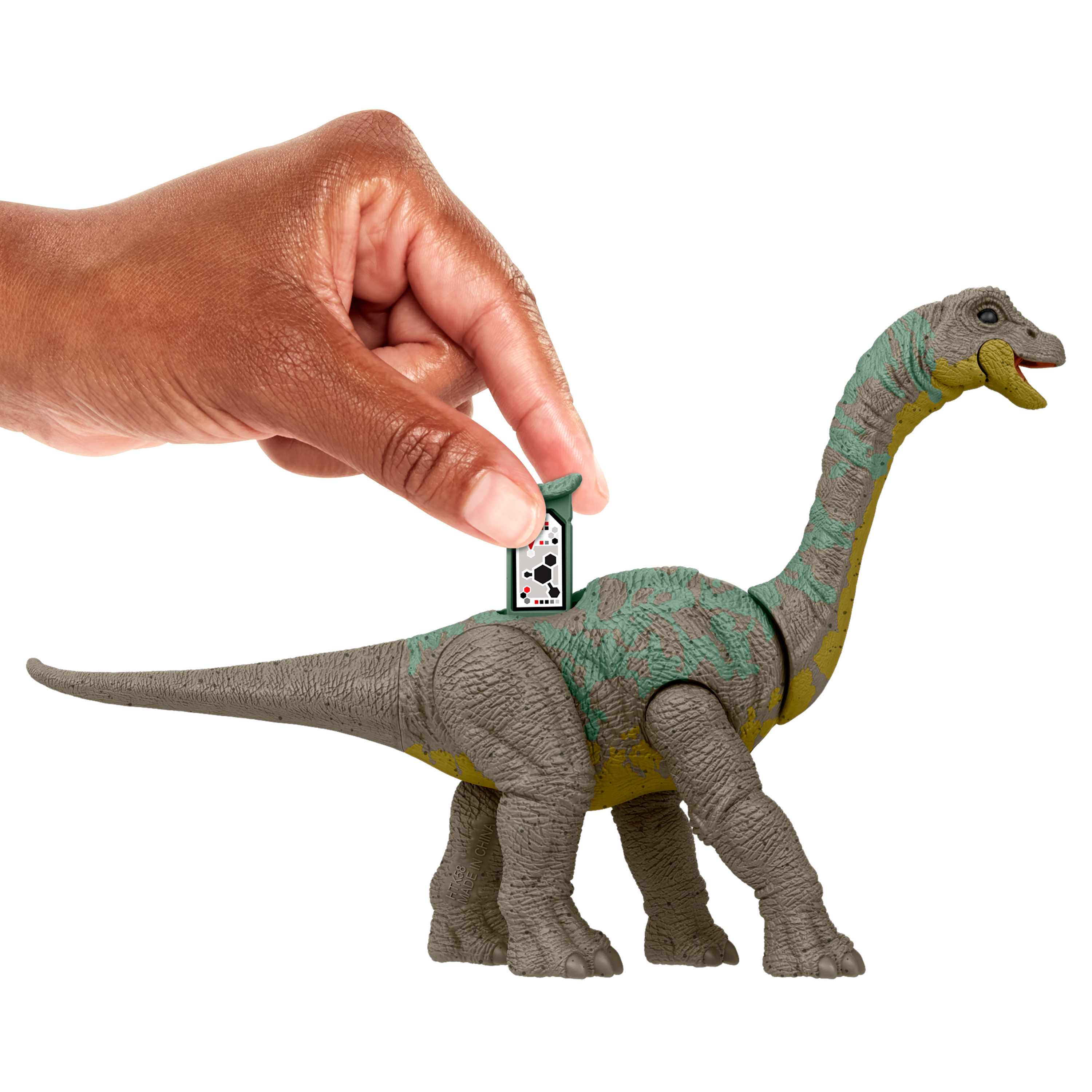 Una mano inserta una tarjeta en la parte posterior de un juguete de dinosaurio. El dinosaurio es gris, con acentos verdes y amarillos.