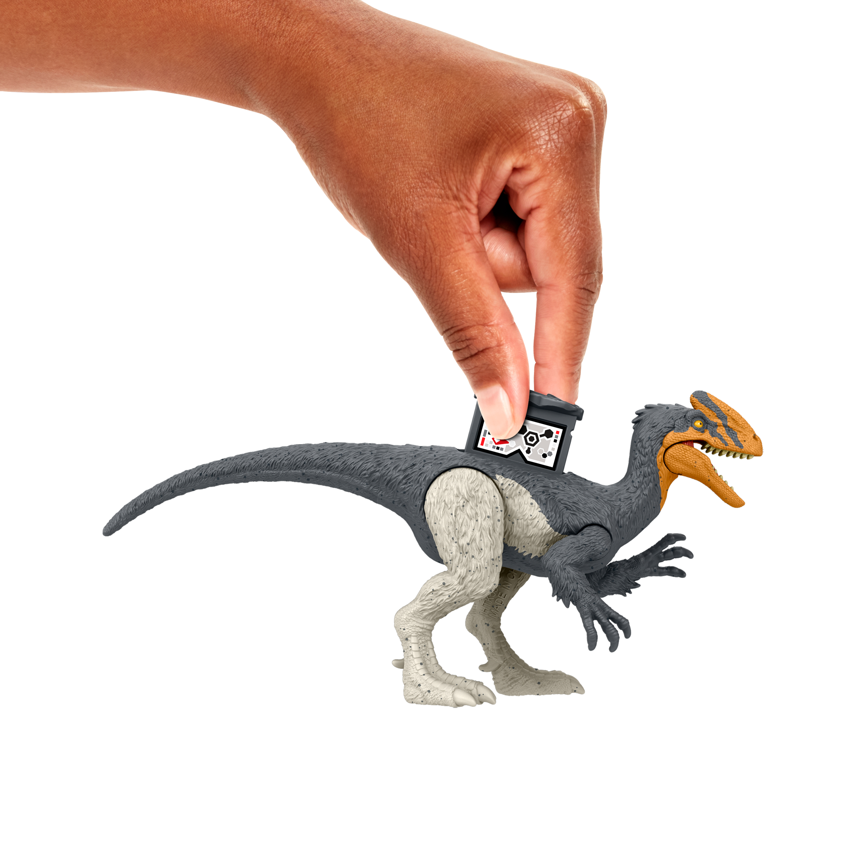 Una mano sostiene un juguete de dinosaurio. El dinosaurio es gris y blanco con la cabeza naranja. Una etiqueta negra está en su espalda.