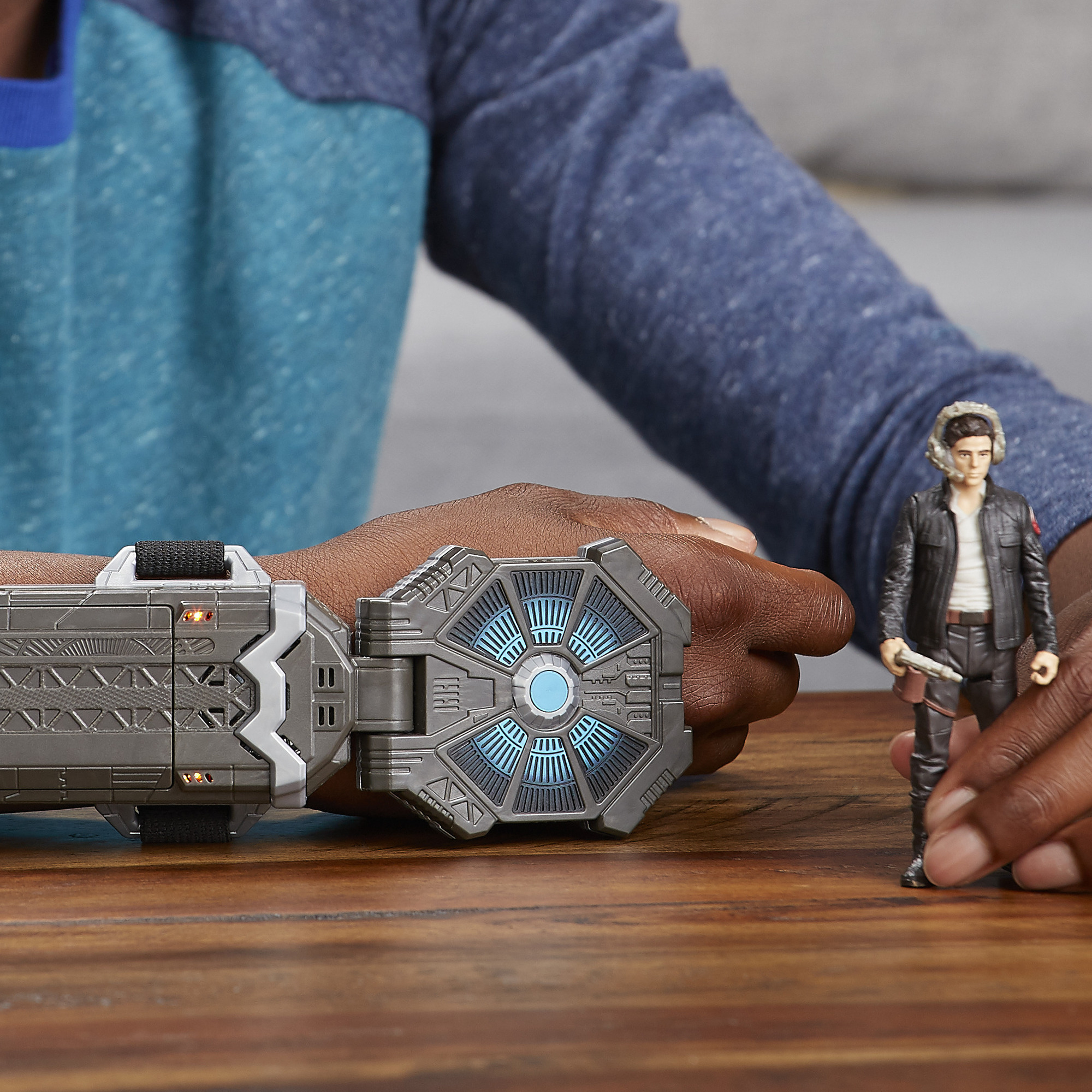 Una persona tiene in mano un giocattolo di Star Wars. Il giocattolo è un dispositivo da polso grigio con luci blu. C'è una statuina di Han Solo.