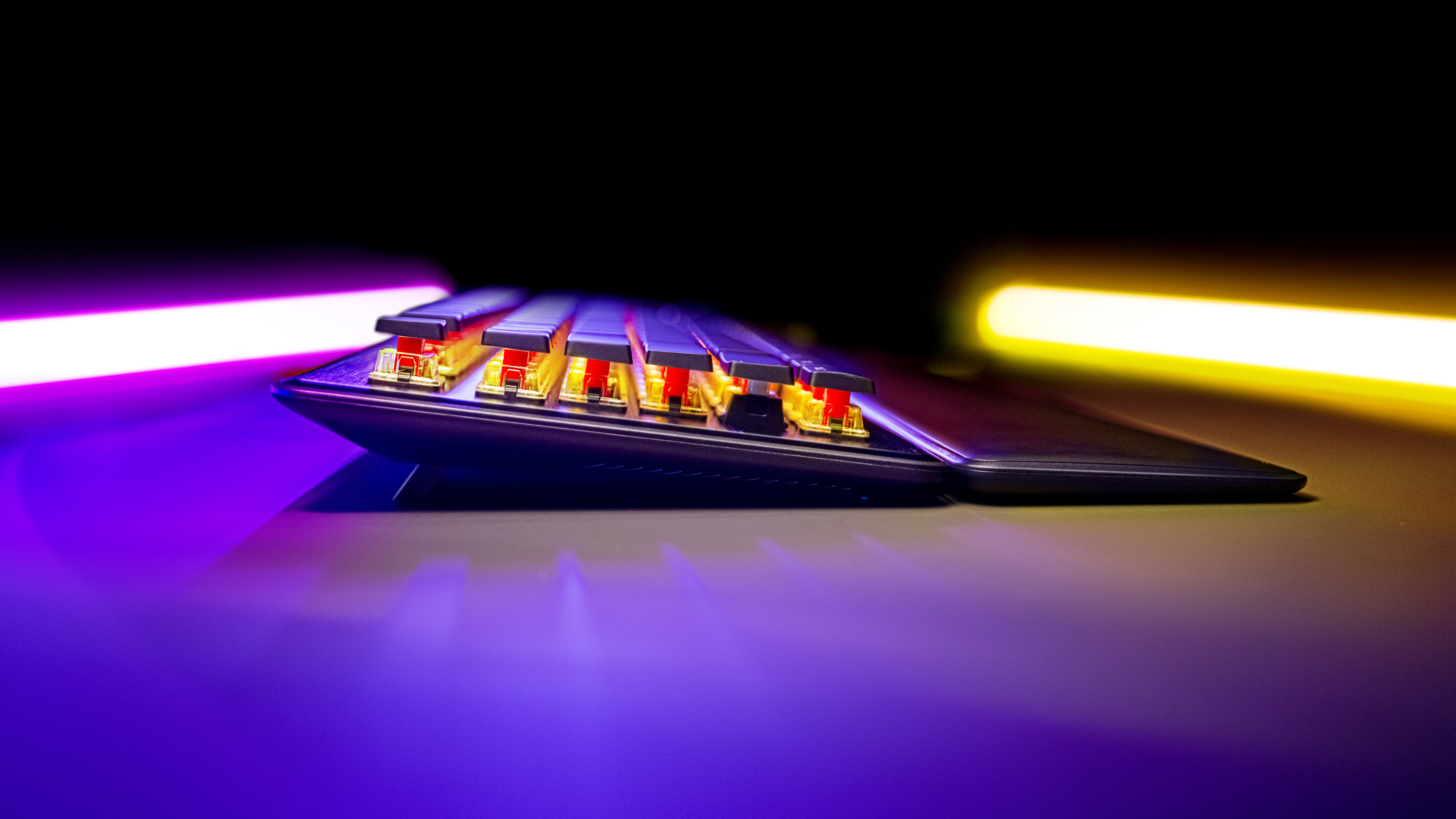 Zbliżenie klawiatury z podświetlanymi klawiszami. Widoczne czerwone przełączniki. Scena ma ciemne tło i fioletowe i żółte światła.
