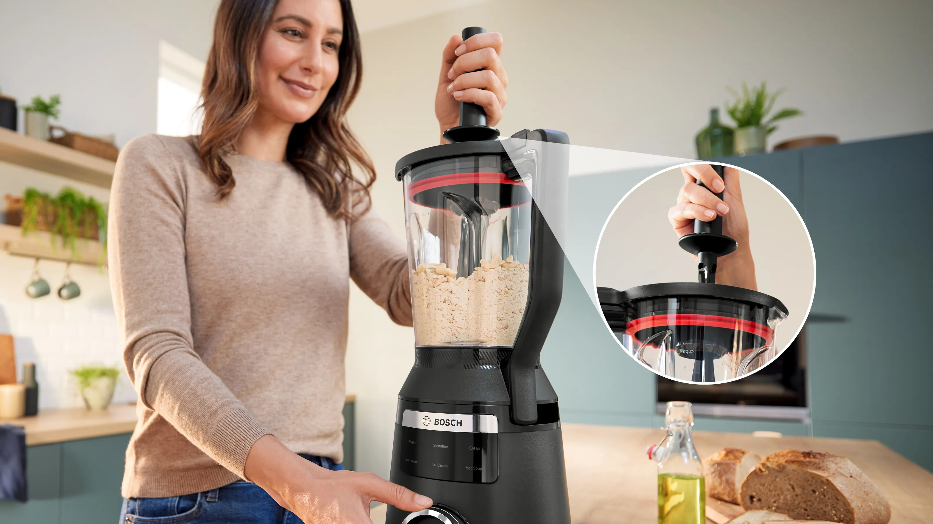 Kobieta używa czarnego blendera Bosch. Blender zawiera jasną substancję. Chleb i olej są na blacie.