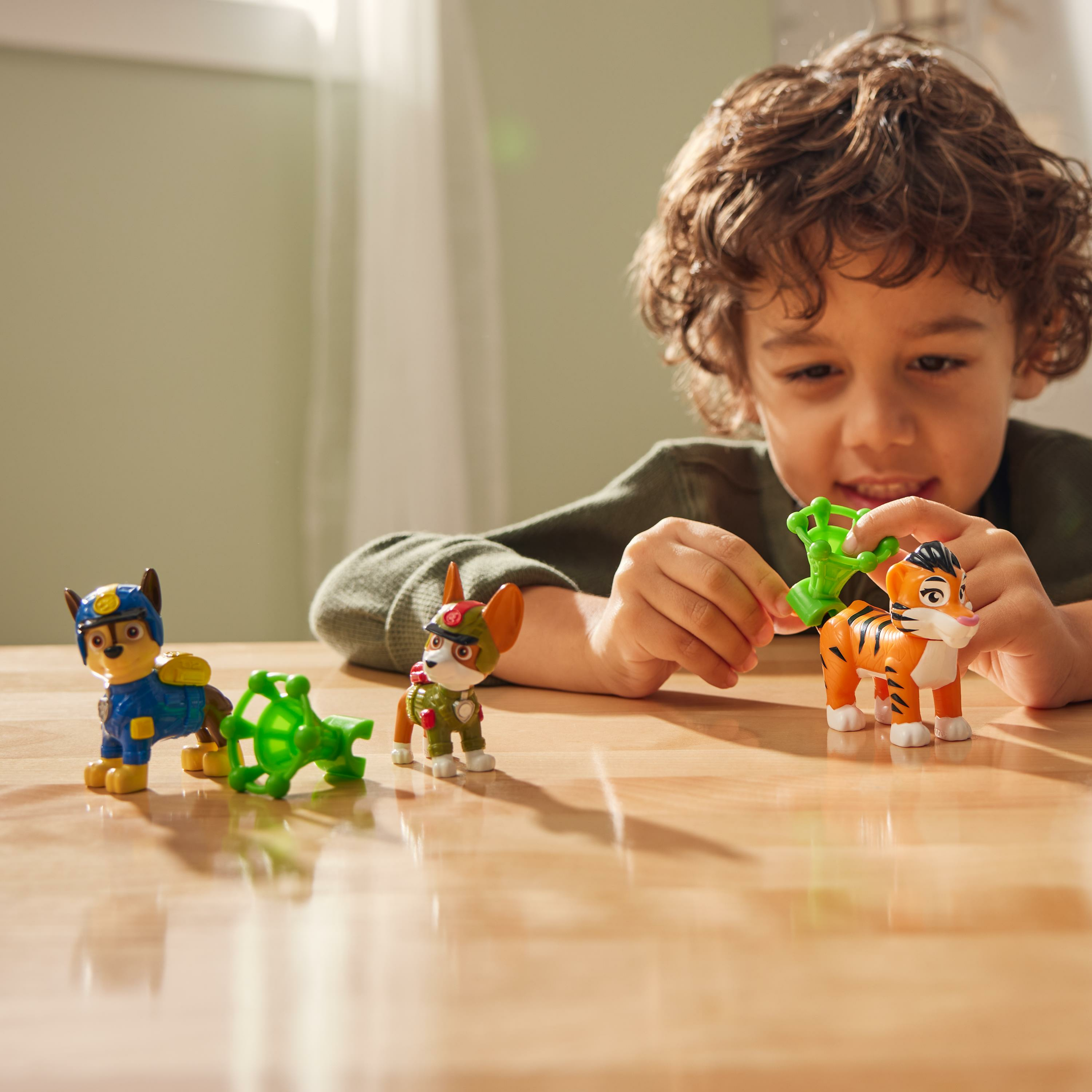 Ein Kind spielt mit Paw Patrol-Spielzeugen. Zu den Spielzeugen gehören Hundefiguren und ein Tiger. Sie stehen auf einem Holztisch.