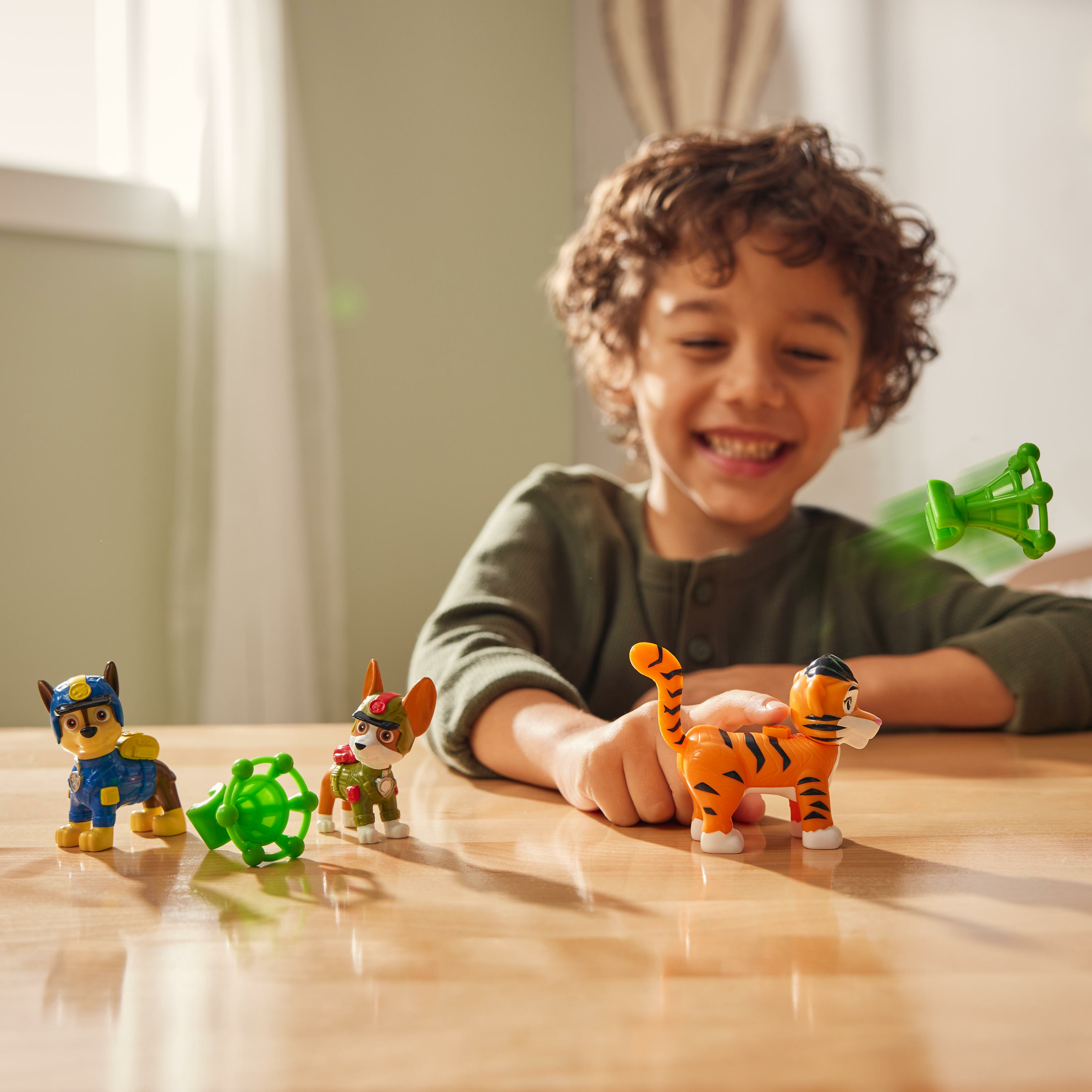 Ein lächelnder Junge mit Spielzeug auf einem Tisch. Paw Patrol und ein Tiger-Spielzeug sind sichtbar.