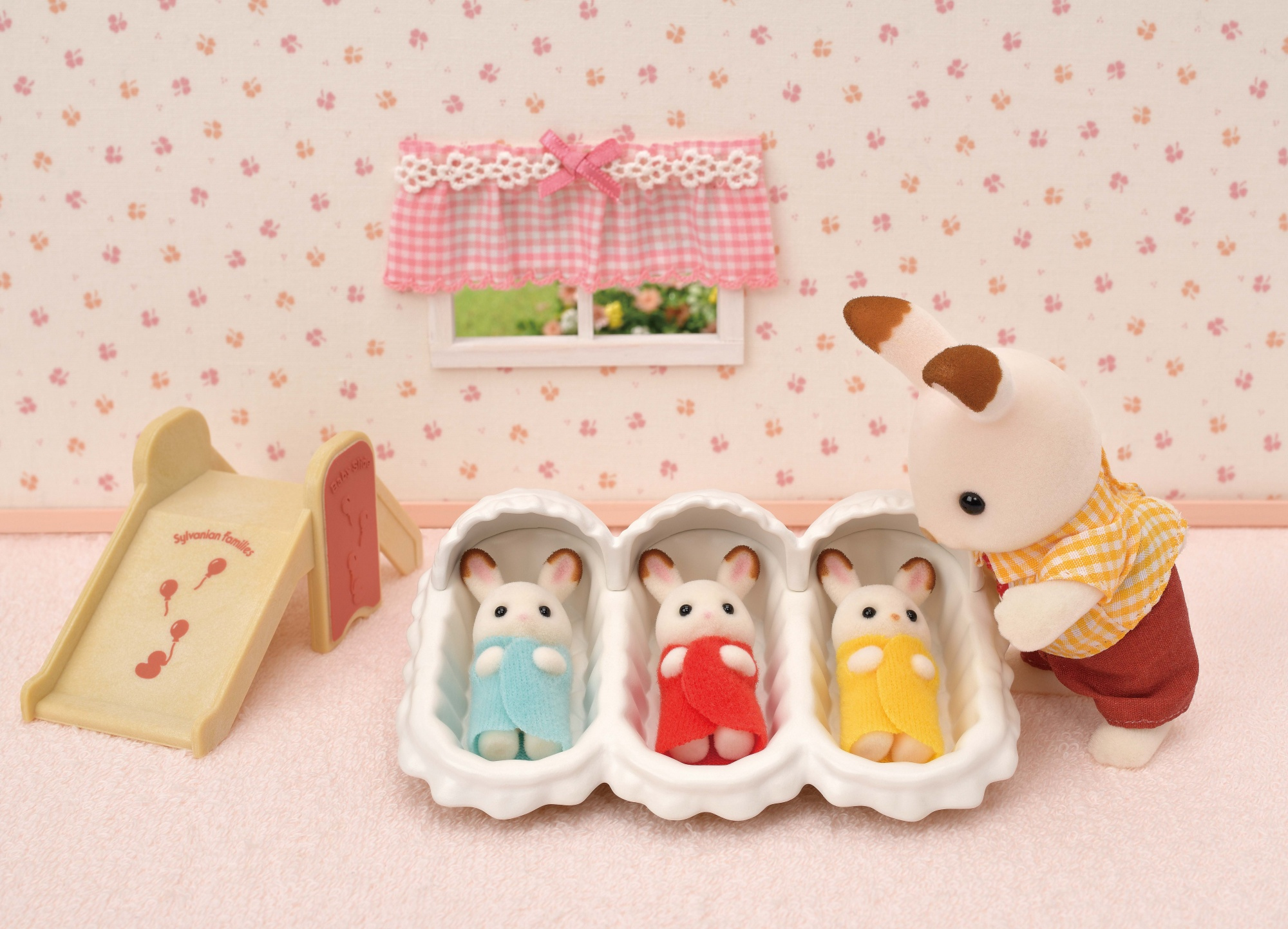 Scena z Sylvanian Families z trzema króliczkami w kołysce, zjeżdżalnią i królikiem rodzicem, który się nimi opiekuje.