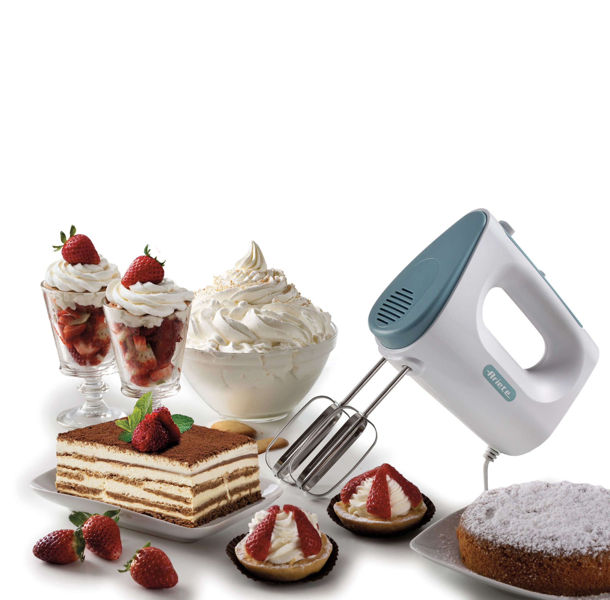 Una batidora de mano blanca y turquesa está junto a postres como tiramisú, tartaletas de fresa y un pastel, todo sobre una superficie blanca.