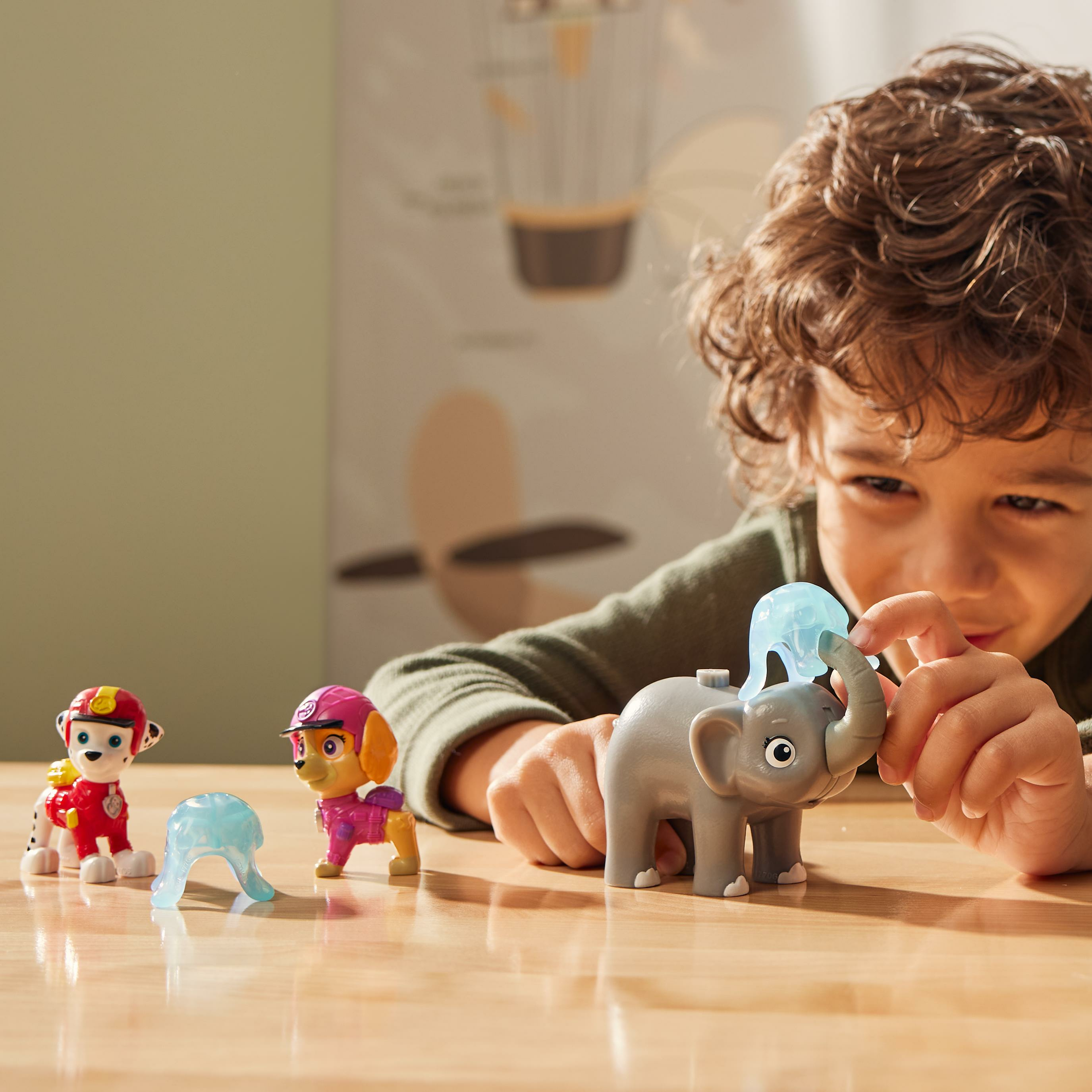 Un bambino gioca con giocattoli, tra cui un elefante grigio e personaggi di Paw Patrol, su una superficie di legno.
