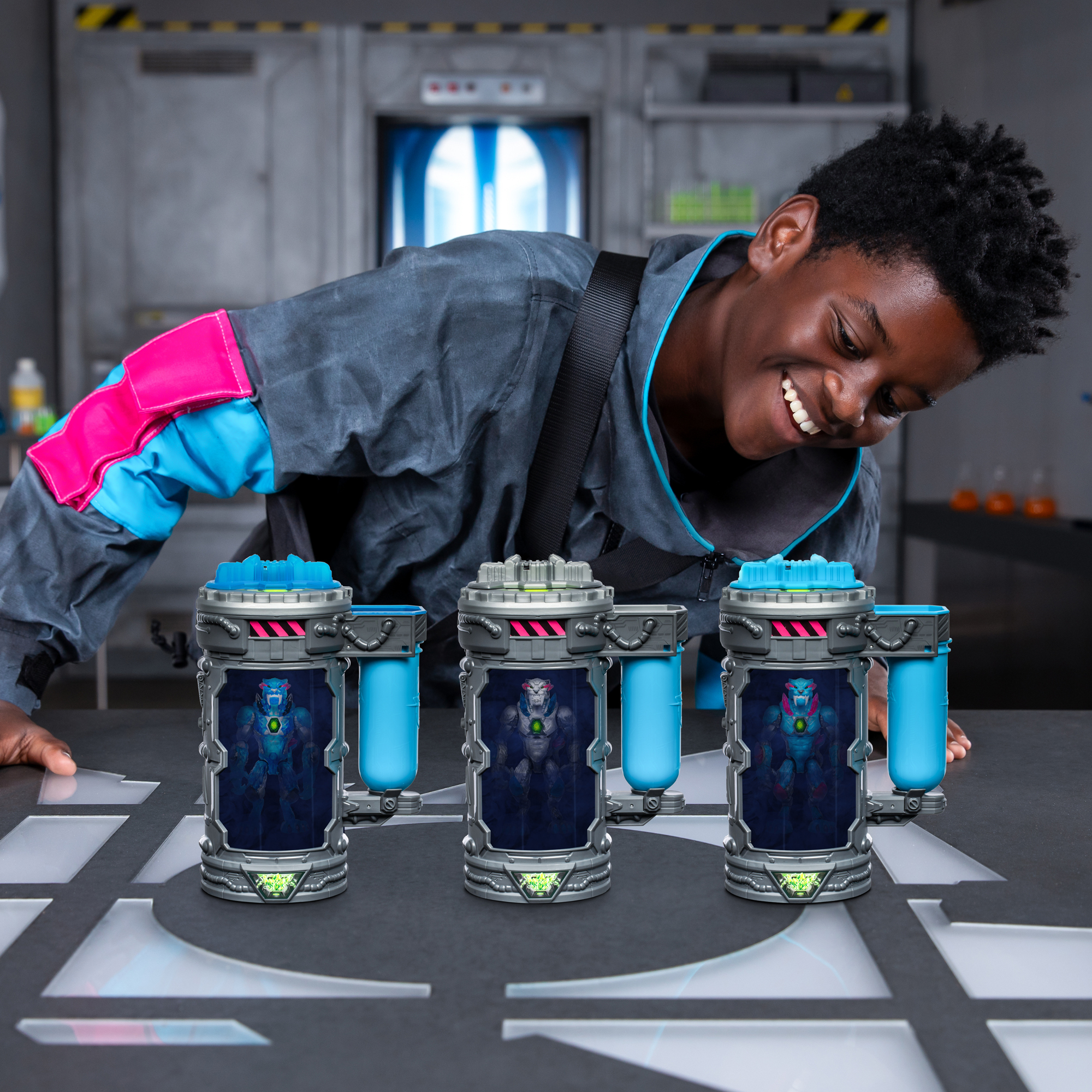 Uśmiechnięty chłopiec patrzy na trzy futurystyczne pojemniki, każdy z figurką robota w środku. Tło sugeruje środowisko laboratoryjne.
