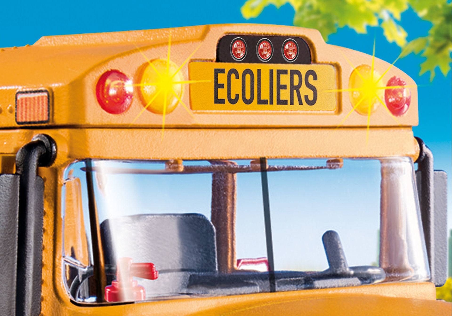 Zbliżenie na przód żółtego autobusu szkolnego. Z przodu napis 'ECOLIERS'. Światła są włączone, z niebieskim niebem w tle.
