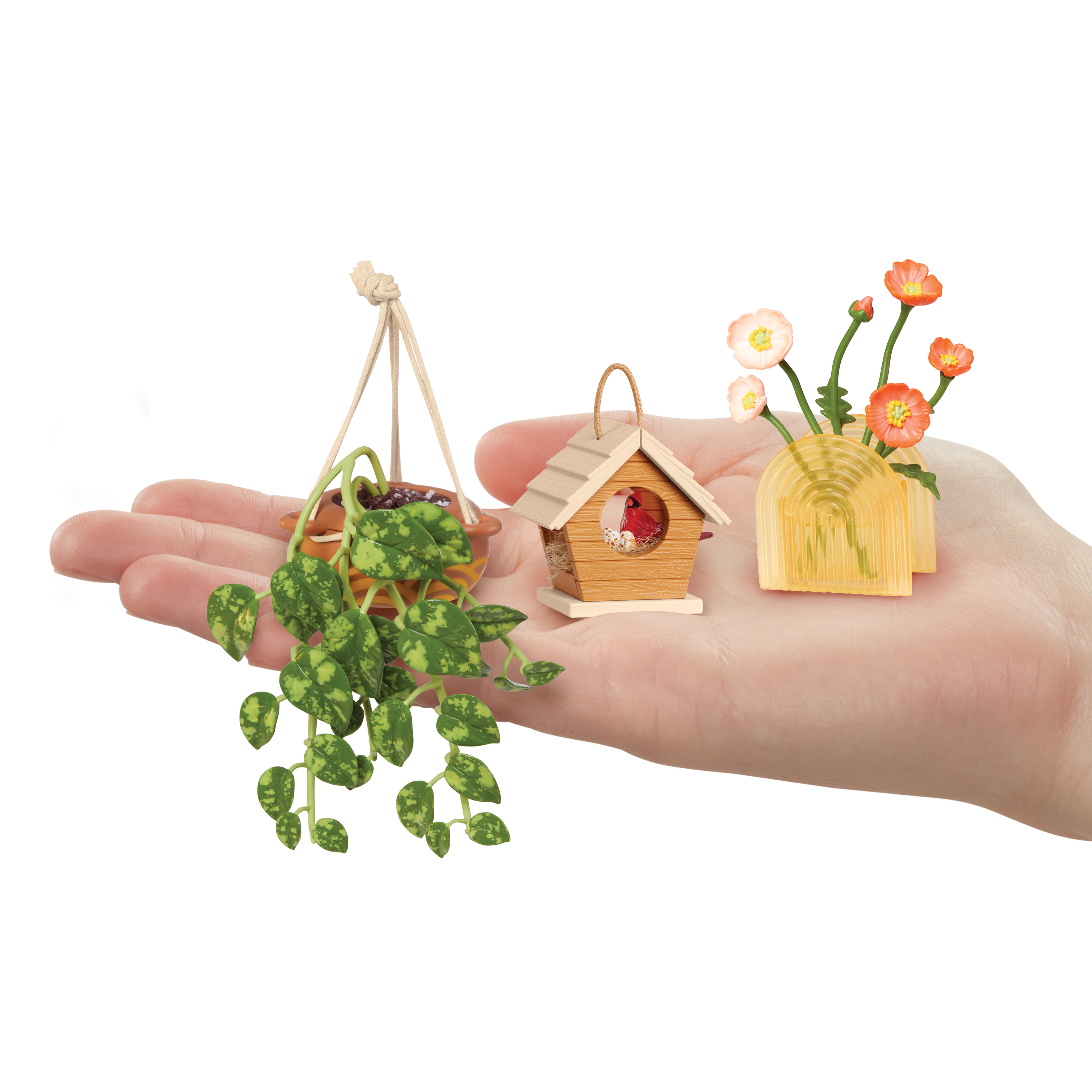 Dłoń trzyma miniaturowe rośliny: wiszącą roślinę, domek dla ptaków z ptakiem i kwiatami w wazonie.