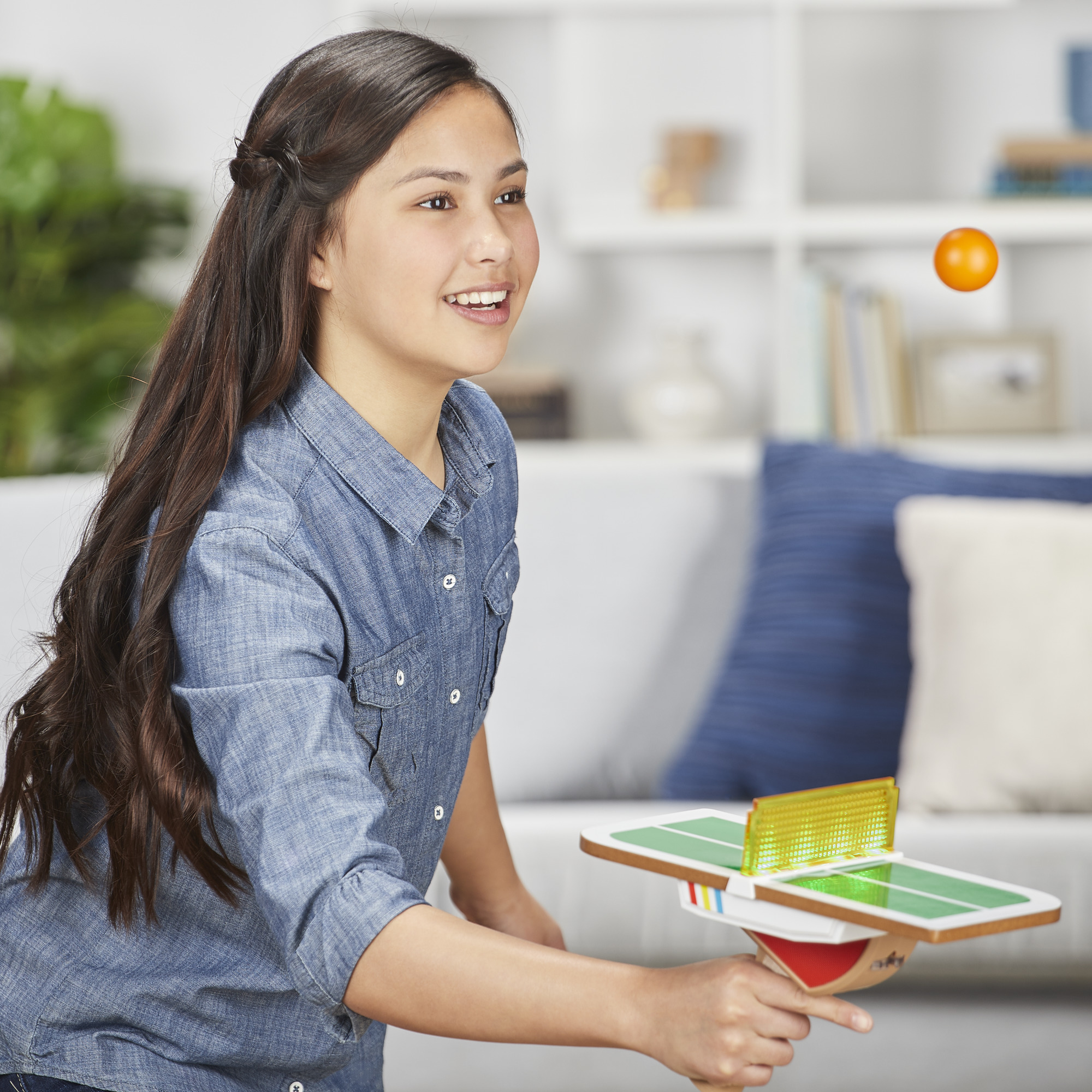 Una ragazza gioca a ping pong. Sorride, tenendo una racchetta con una rete. Una palla arancione è a mezz'aria.