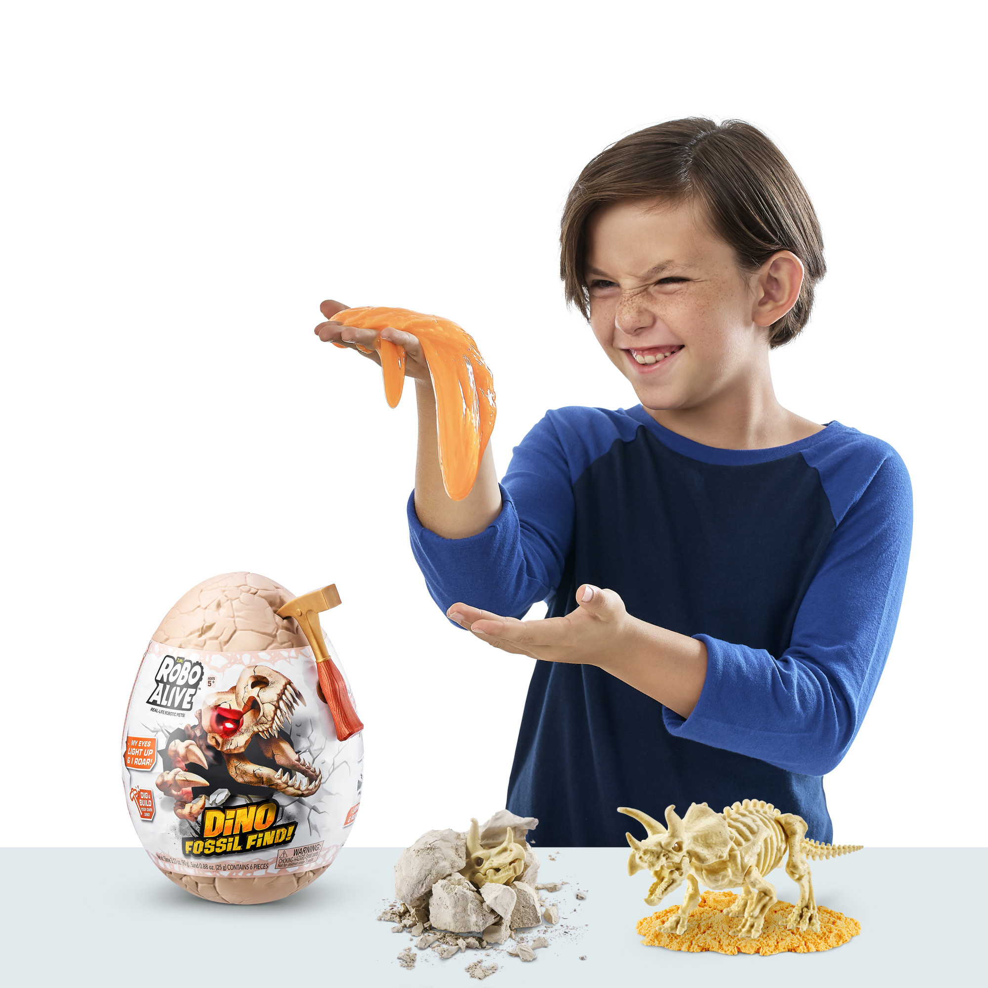 Een jongen houdt oranje slijm vast. Een Dino-fossielenkit met een gebroken ei, fossielen en een dinosaurus skelet op tafel.