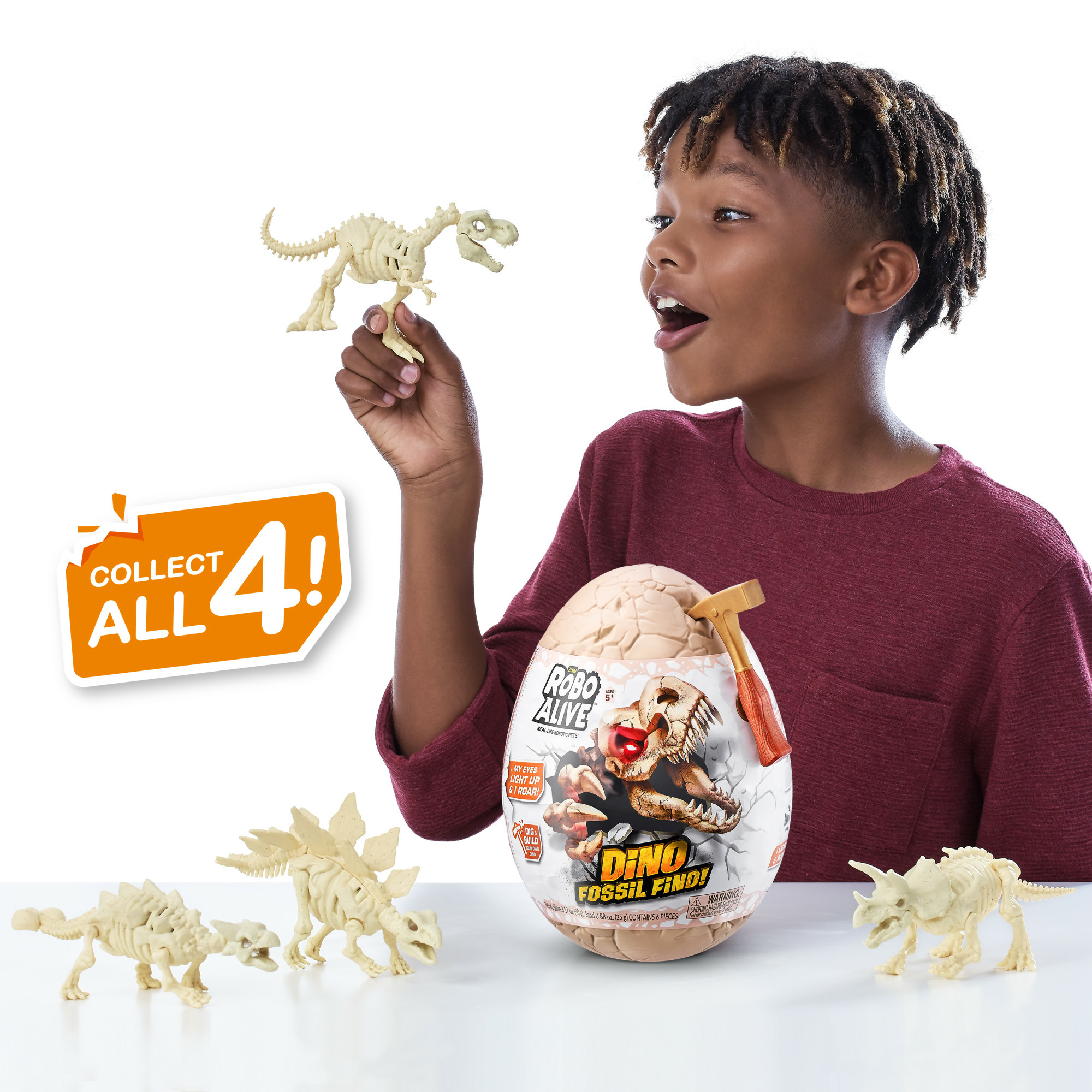 Een jongen houdt een speelgoed dinosaurus skelet vast. Een eivormig speelgoed en andere dinosaurus skeletten op een wit oppervlak.