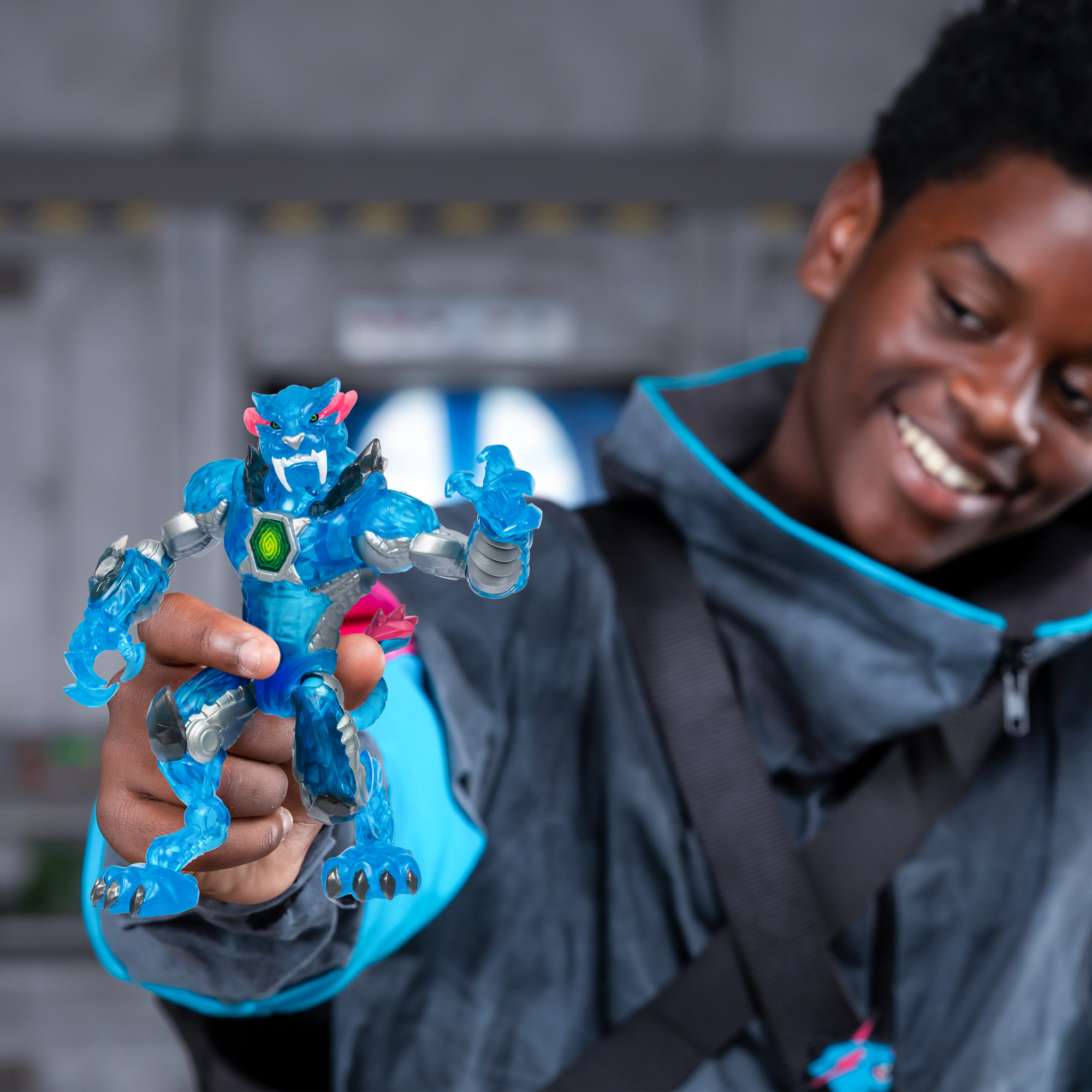 Ein Teenager hält eine blaue Actionfigur. Die Figur hat ein katzenartiges Gesicht mit rosa Akzenten. Der Teenager lächelt vor einem verschwommenen Hintergrund.