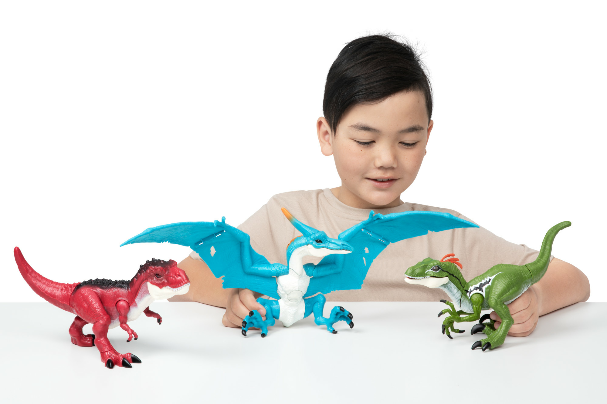 Un ragazzo con giocattoli di dinosauri. Dinosauri giocattolo rossi, blu e verdi sono sul tavolo bianco. Il ragazzo sorride.