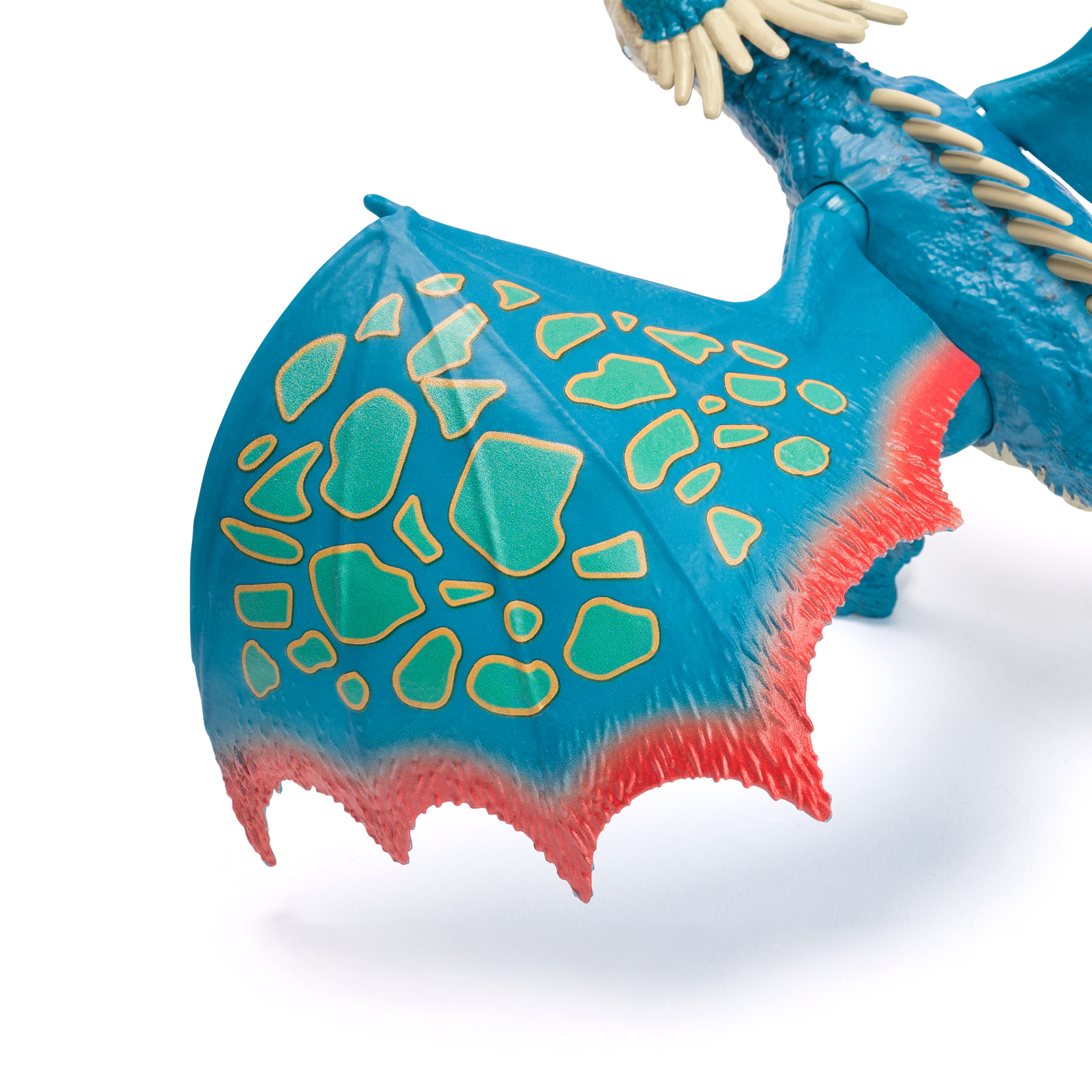 Niebieska zabawka smoka ze skrzydłem we wzory, zielonymi plamami i czerwonymi krawędziami na białym tle.