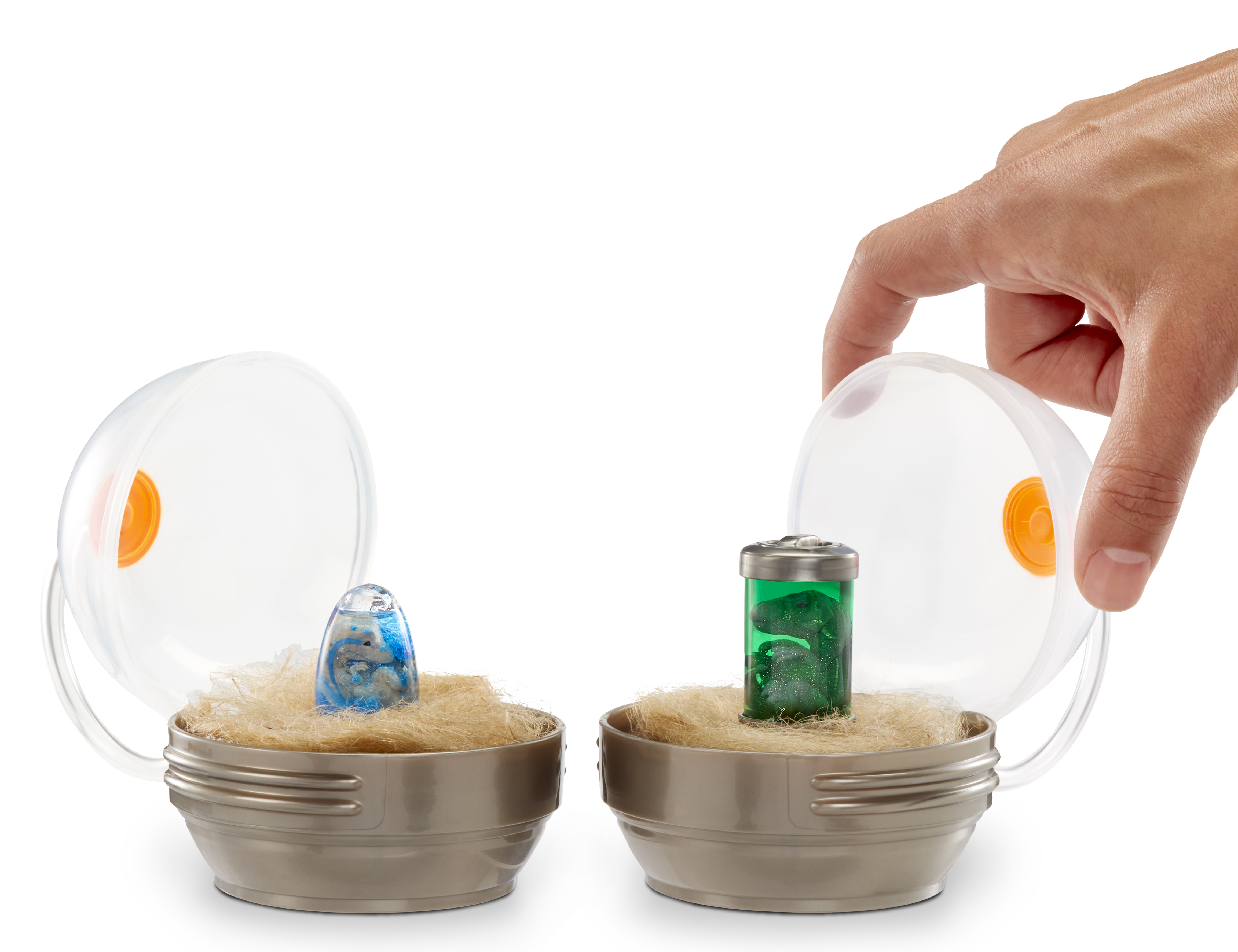 Dwa pojemniki z przedmiotami. Ręka trzyma pokrywkę. Jeden ma niebieski przedmiot, drugi zielonego dinozaura.