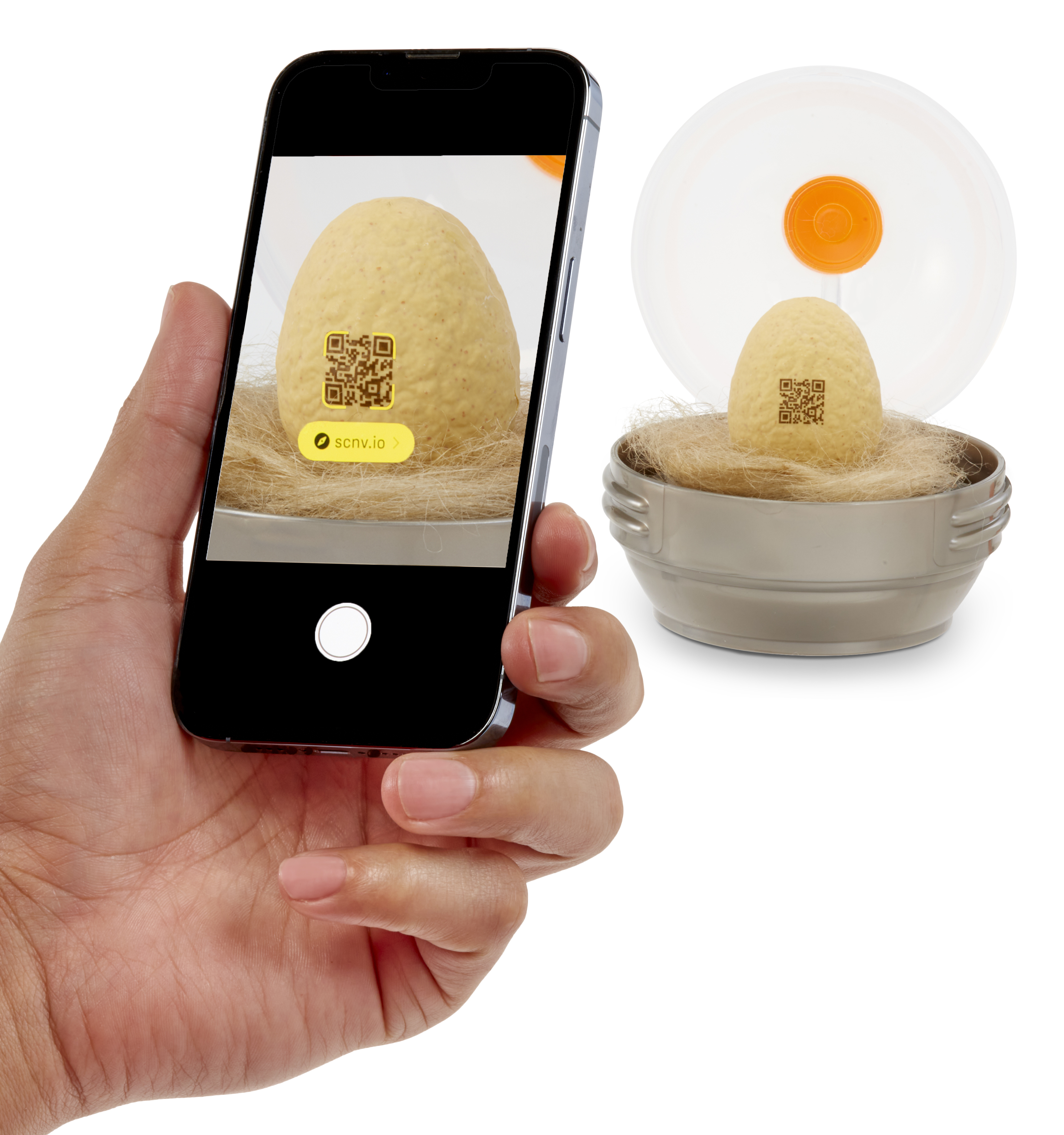 Ręka trzymająca telefon skanujący jajko z kodem QR. Kolejne jajko jest w misce ze słomą.