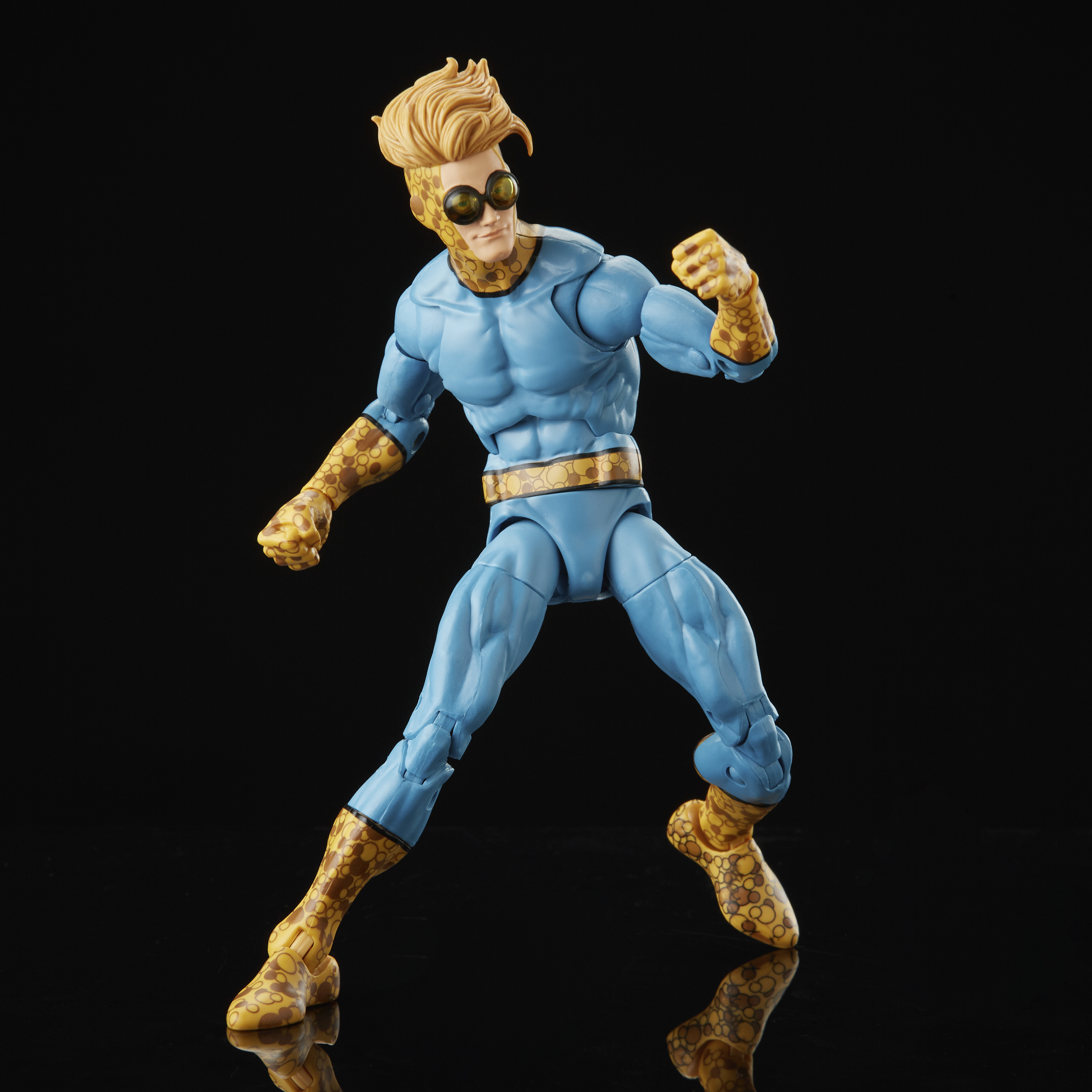 Figura de acción de superhéroe. Traje azul, brazos/piernas amarillas con manchas, pelo rubio y gafas de sol. Superficie negra reflectante.