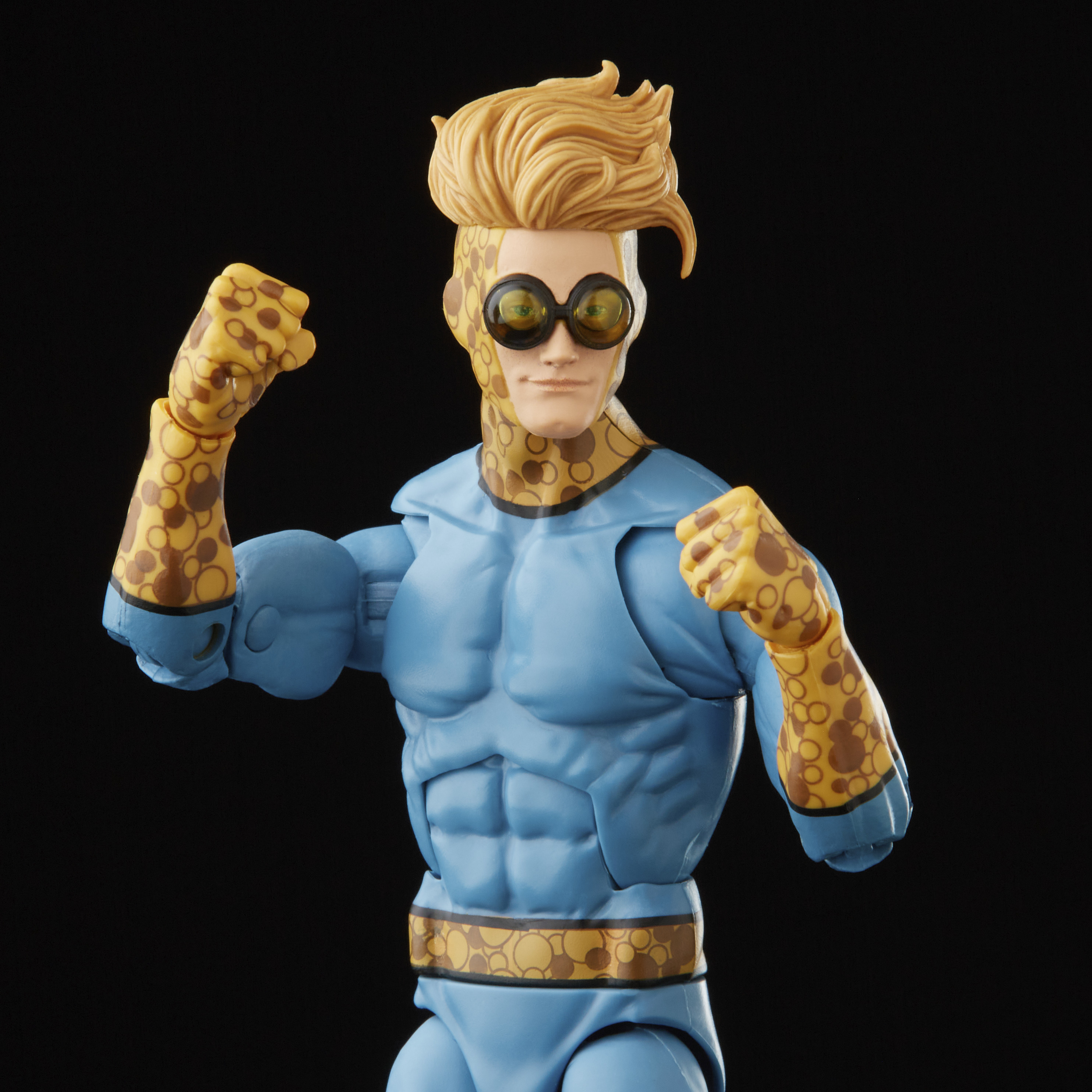 Una figura de acción de superhéroe. Cabello rubio, gafas y brazos manchados. Traje azul, puños apretados, fondo negro.