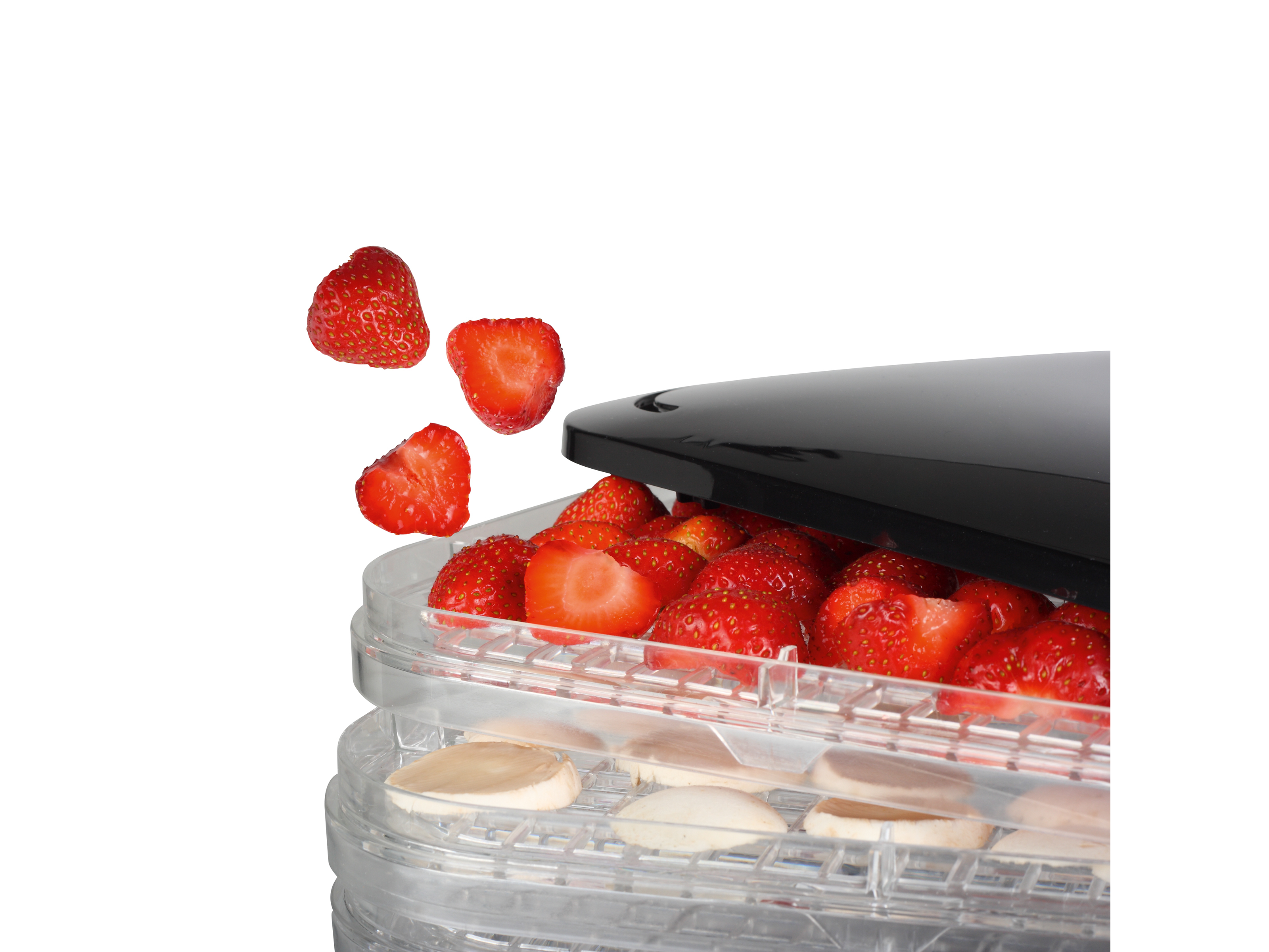 Truskawki wpadają do suszarki do żywności. Widoczne są pokrojone i całe jagody. Plastry suszą się na dolnej tacy.