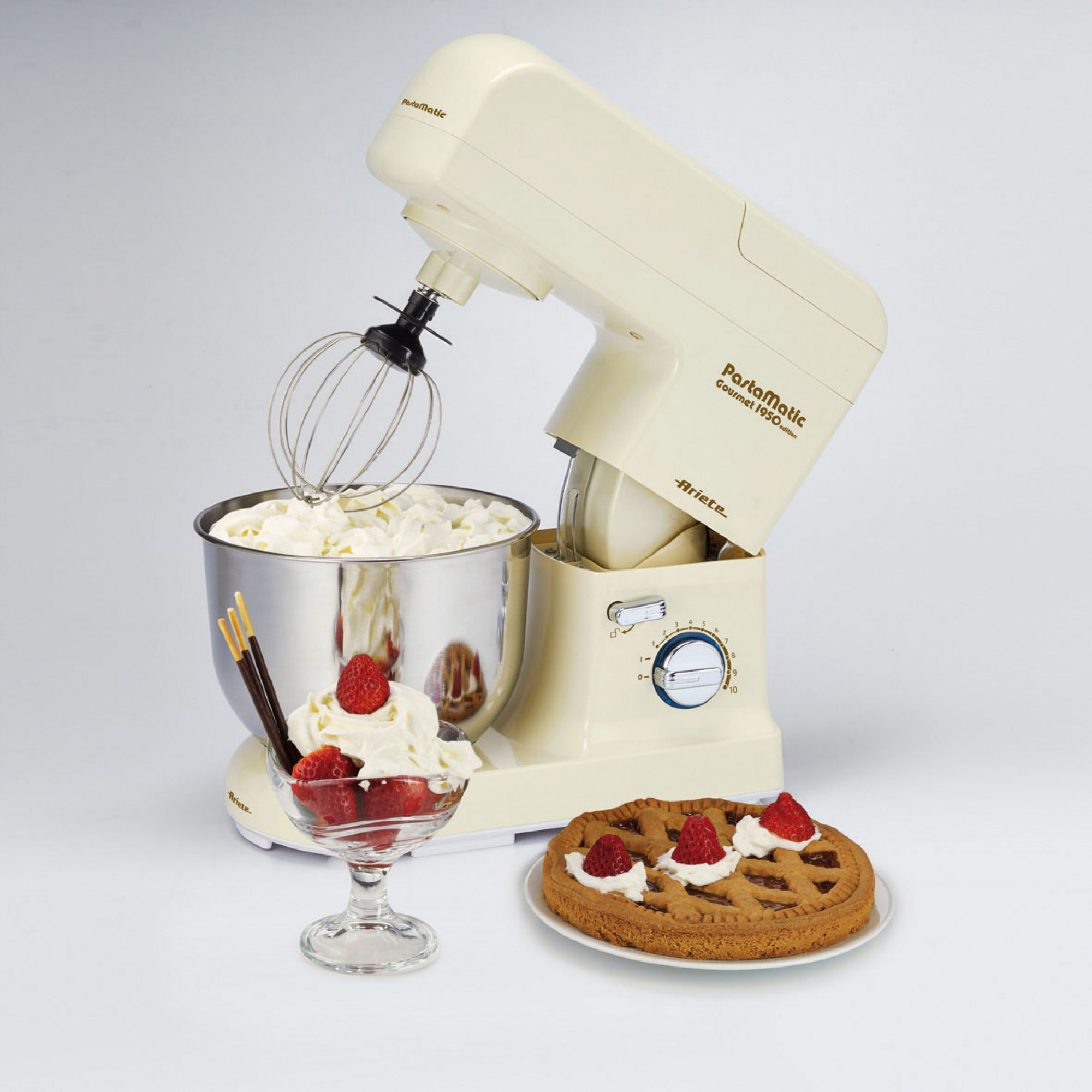 Batidora color crema con tazón de crema batida, postre con fresas y pastel con crema y fresas.
