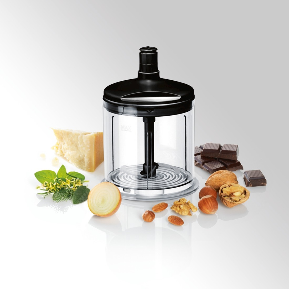 Un procesador de alimentos con ingredientes como queso, hierbas, cebolla, chocolate y nueces dispuestos sobre una superficie blanca.