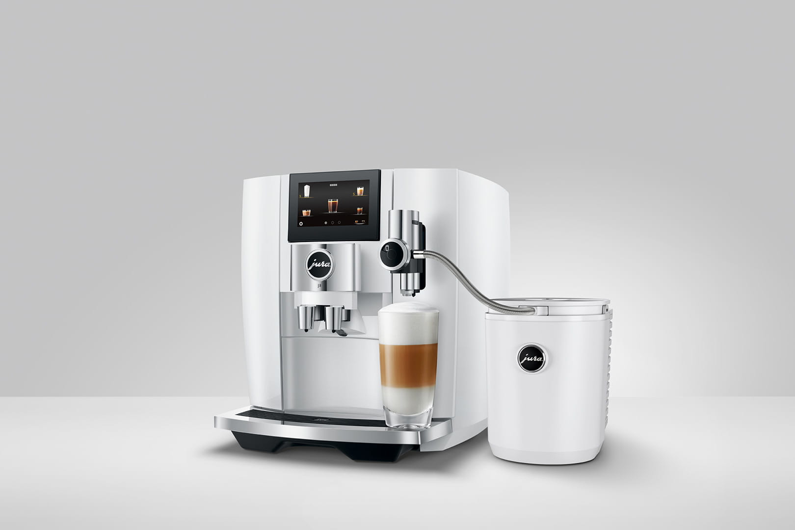 Una macchina da caffè Jura bianca con un bicchiere di latte macchiato. È su una superficie bianca.