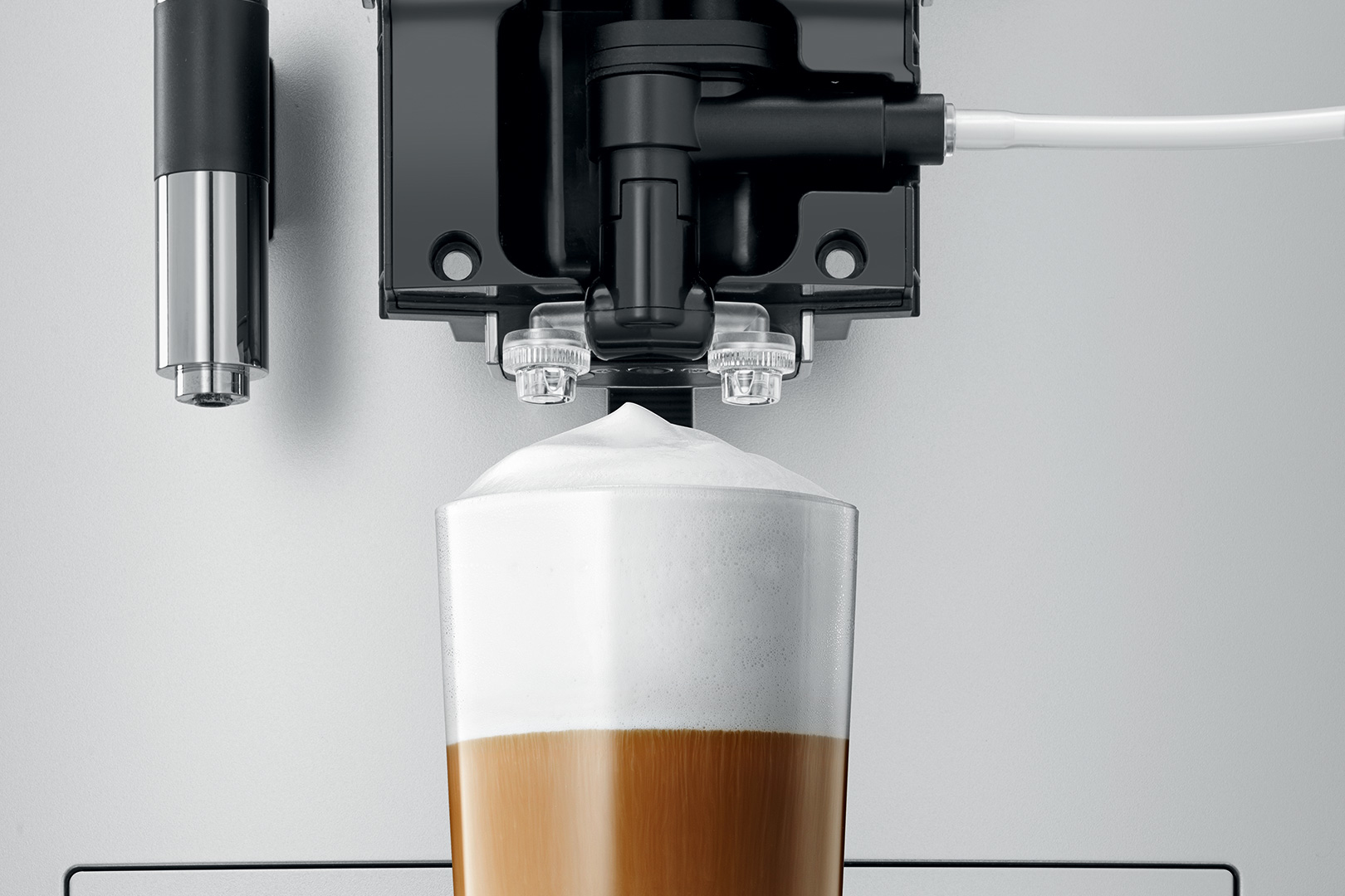 Eine Kaffeemaschine gibt einen Latte Macchiato aus. Das Getränk ist geschichtet mit Kaffee und Schaum. Maschinenteile sind schwarz und silber.