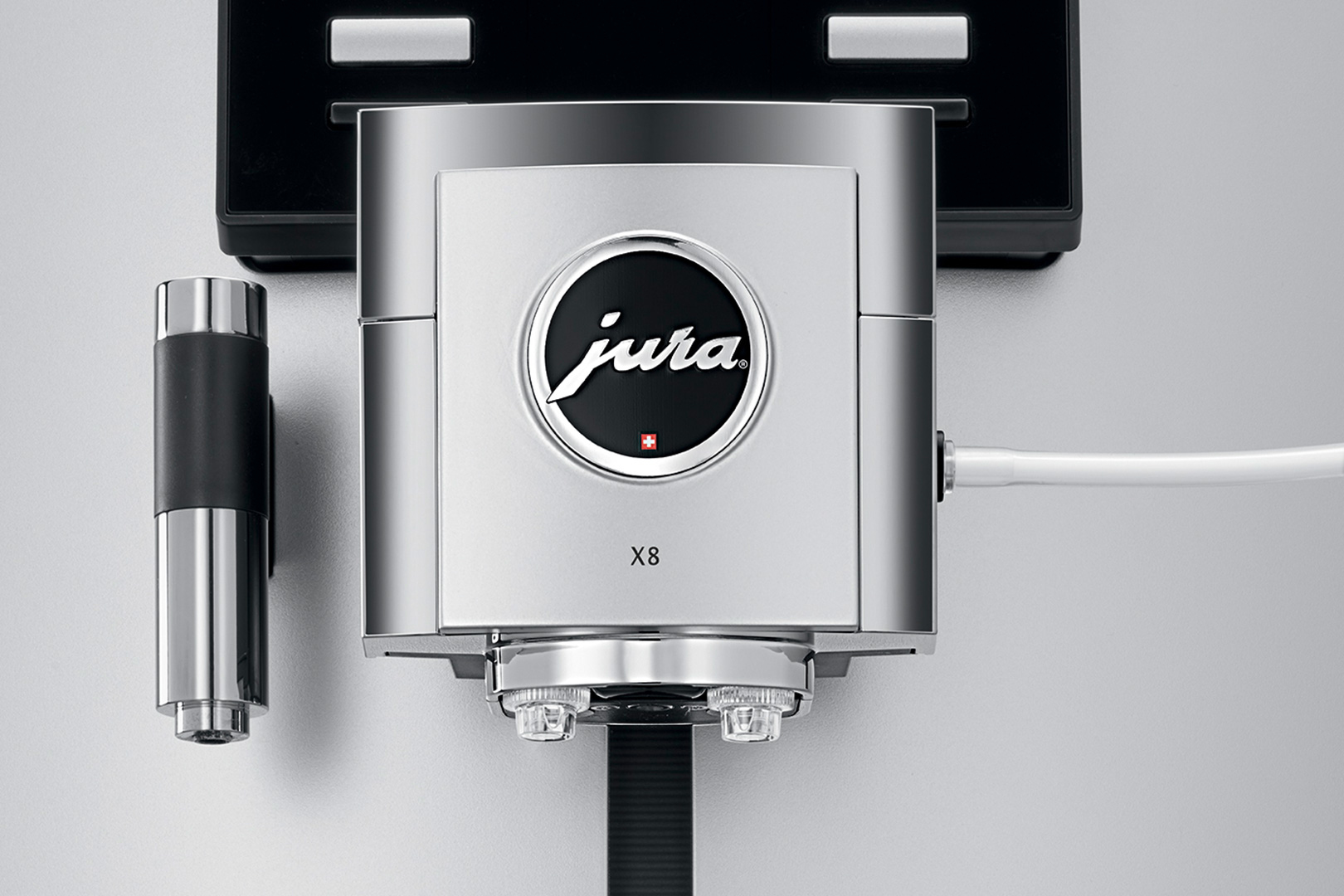 Nahaufnahme einer silbernen Jura X8 Espressomaschine. Sie hat ein schwarzes Logo mit 'Jura' und einem roten Kreuz. Ein schwarzes Rohr ist sichtbar.