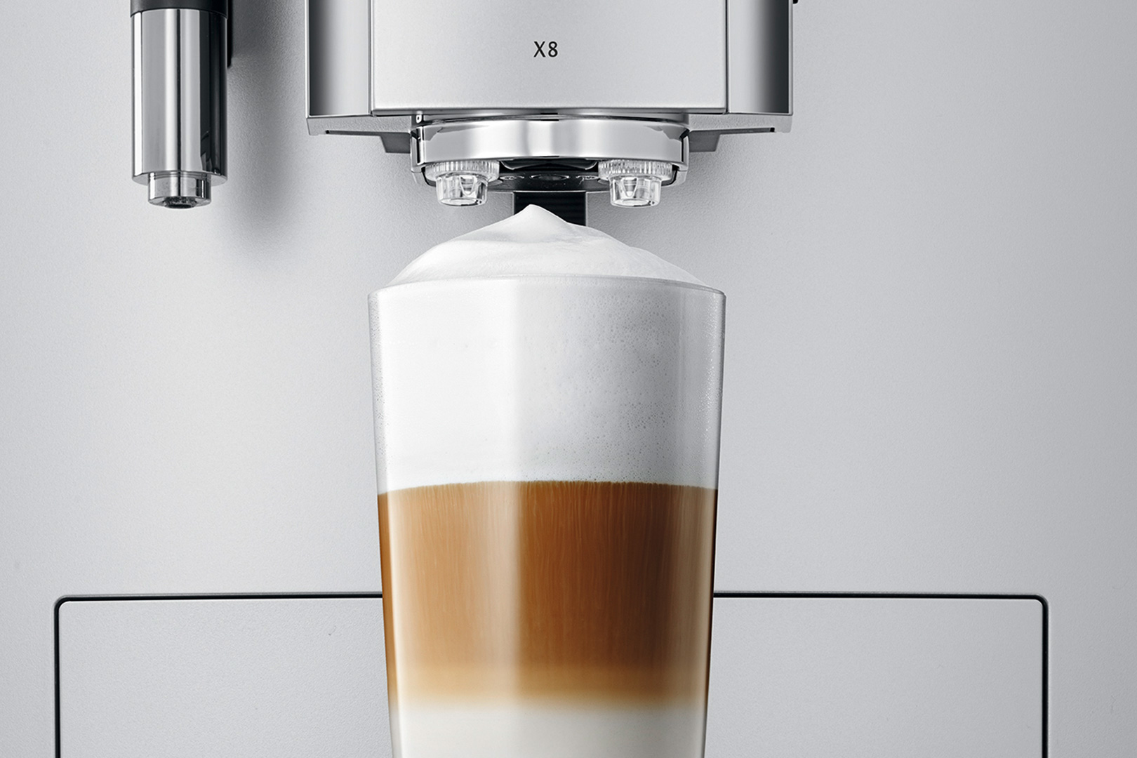 Eine Kaffeemaschine gibt einen geschichteten Latte in ein Glas aus. Das Getränk hat drei verschiedene Schichten und ist mit Schaum bedeckt.