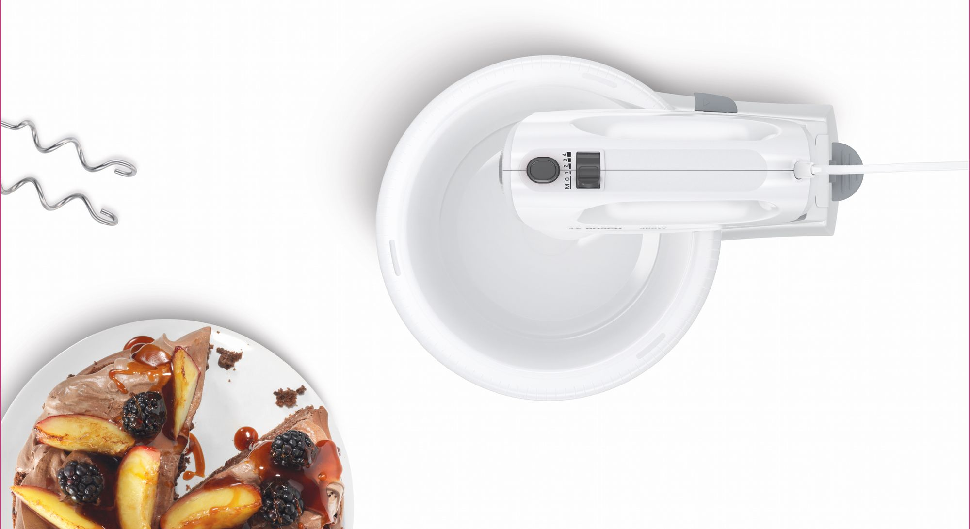 Ein weißer Mixer, eine Schüssel und ein Kuchenstück mit Früchten. Schneebesenaufsätze links. Draufsicht auf weißem Hintergrund.