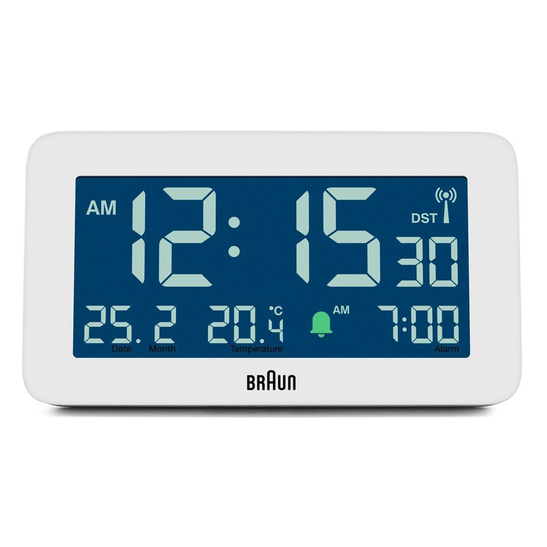Eine weiße digitale Braun-Uhr zeigt 12:15:30 AM, Datum, Temperatur und Weckzeit an. Der Markenname ist sichtbar.