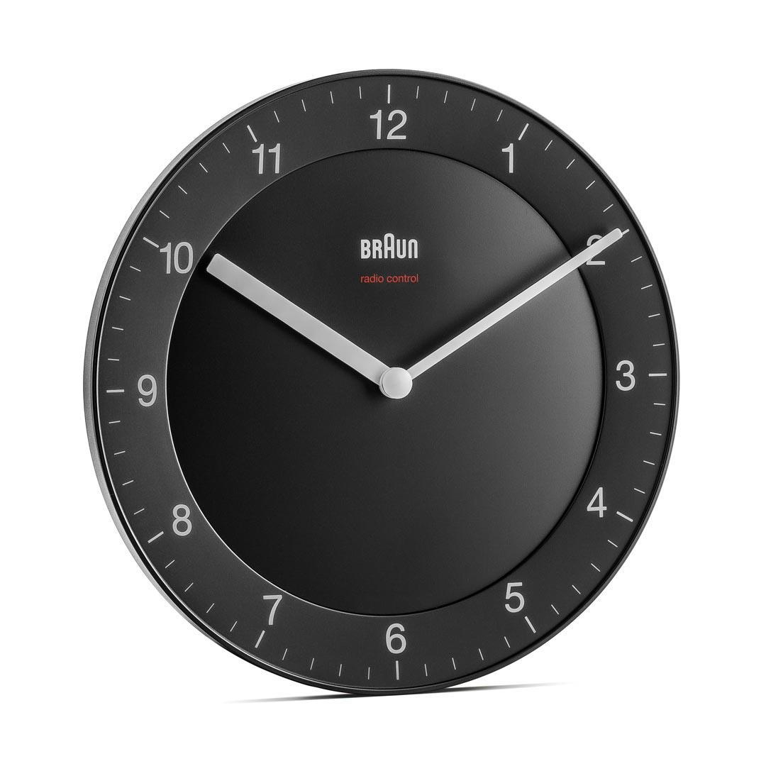 Eine runde, schwarze Braun-Uhr. Weiße Zeiger, Ziffern und Strichmarkierungen. Der Markenname und 'radio control' sind weiß.