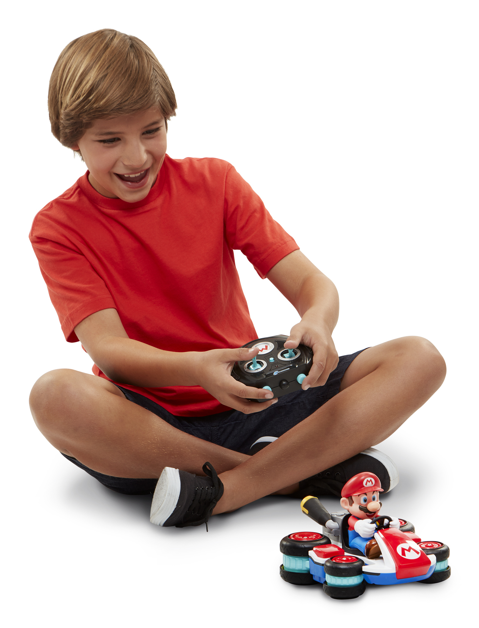 Ein Junge in einem roten Hemd sitzt und spielt mit einem ferngesteuerten Auto mit Mario-Figur. Das Auto steht auf dem Boden.