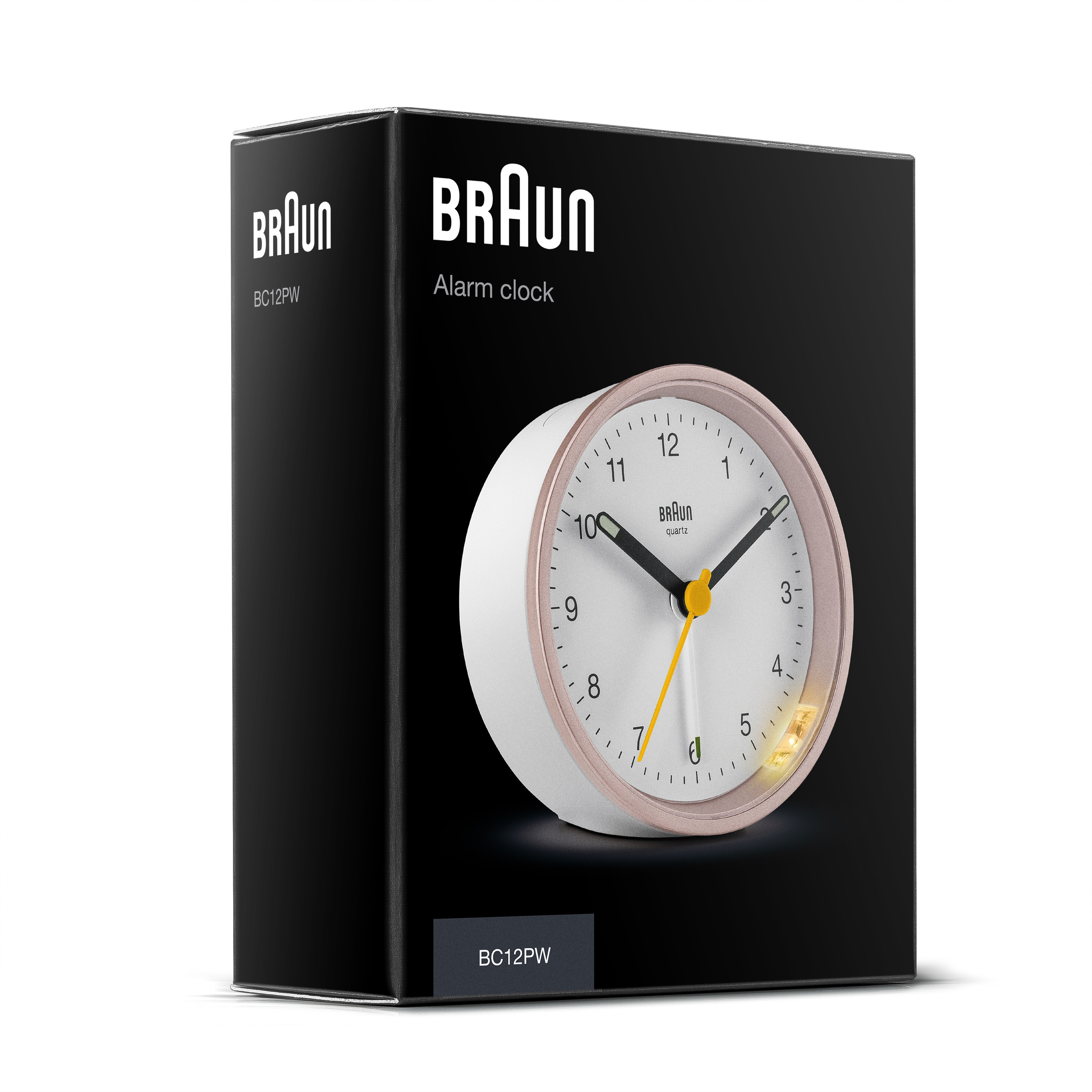 Un réveil Braun dans une boîte noire. L'horloge est blanche avec un anneau or rose. Les aiguilles sont noires et jaunes.