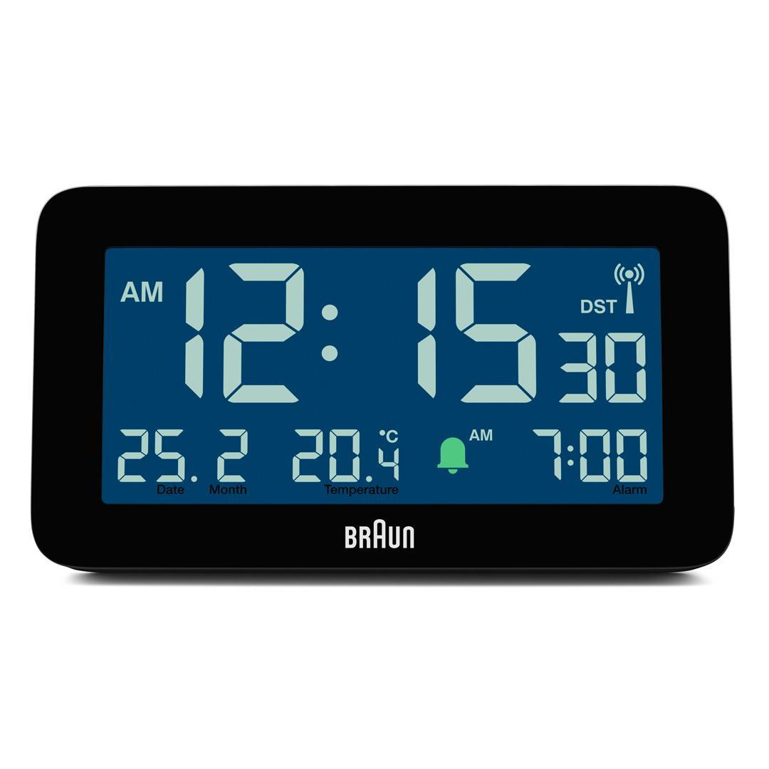 Eine Digitaluhr zeigt 12:15 Uhr an, Datum, Monat, Temperatur und Weckzeit. Die Marke ist Braun.