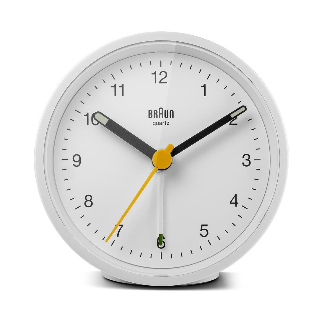 Eine weiße Braun-Quarzuhr, schwarze Zeiger, gelber Sekundenzeiger. Die Uhr zeigt 10:10 Uhr. Der Hintergrund ist weiß.