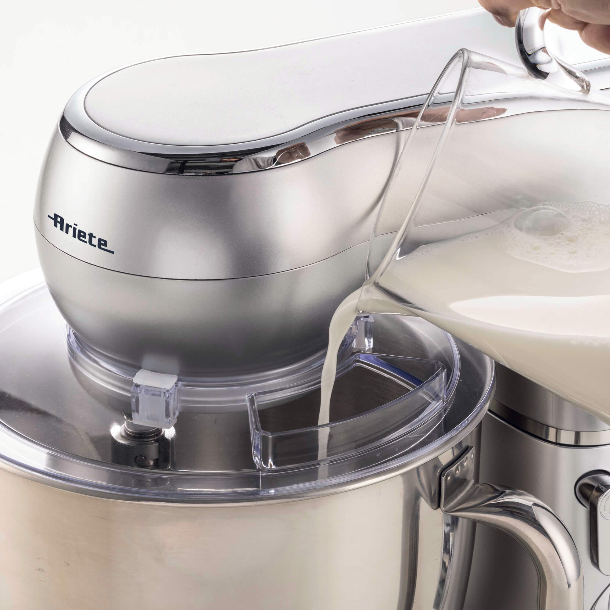 Eine Hand gießt Milch aus einem Glaskrug in eine silberne Eismaschine.
