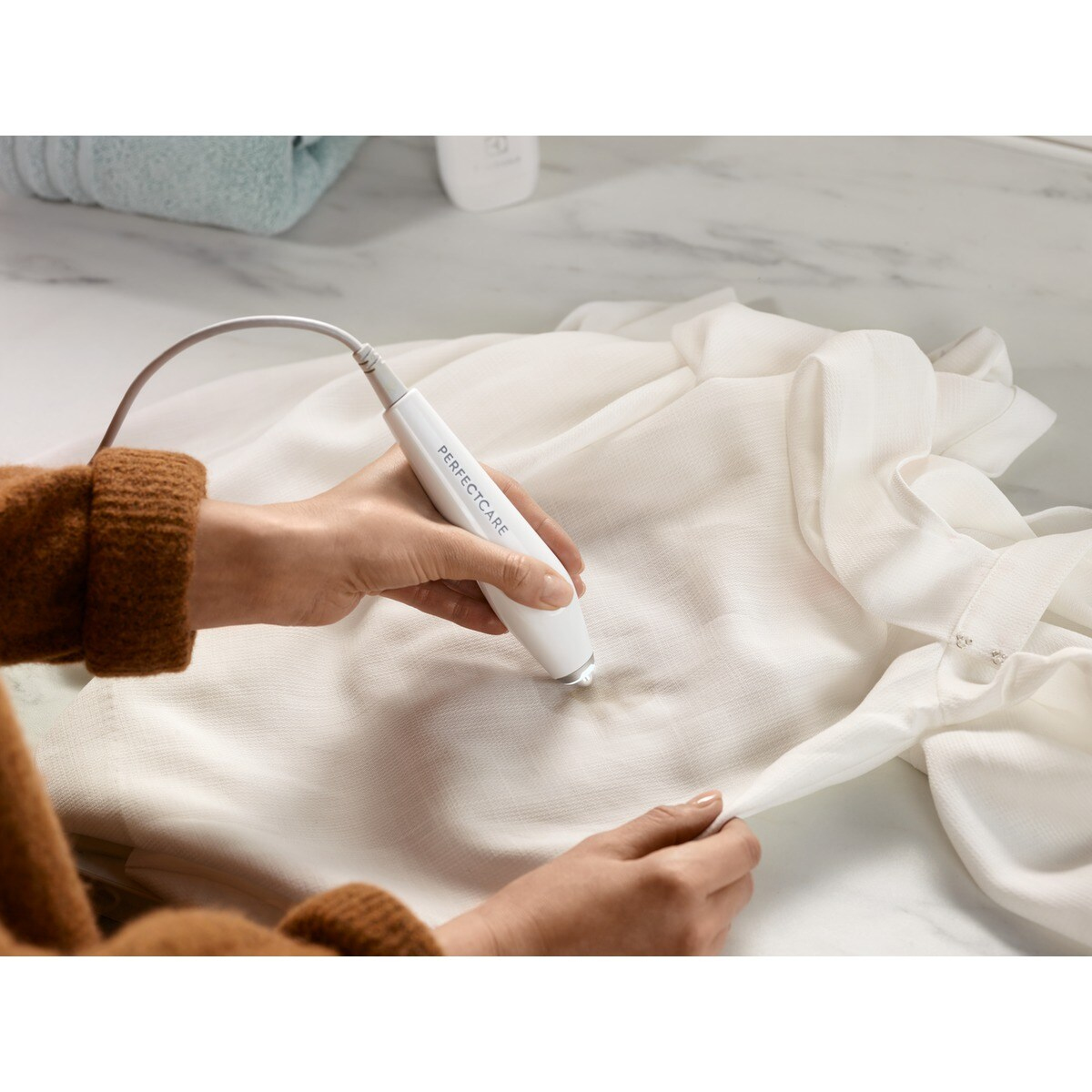Osoba używa białego urządzenia Perfectcare na białym ubraniu. Urządzenie jest trzymane nad plamą.