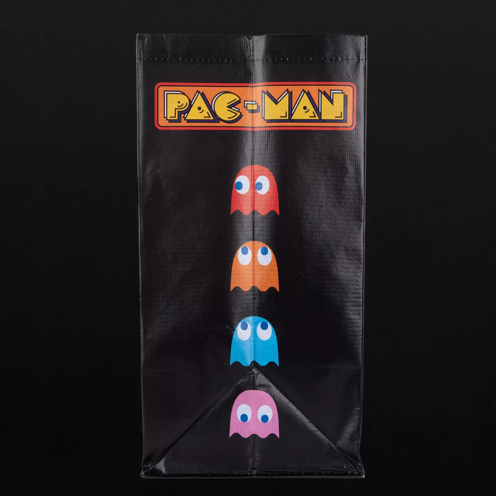 Eine schwarze Pac-Man-Tasche mit dem Pac-Man-Logo und vier farbigen Geistern: rot, orange, blau und rosa auf schwarzem Hintergrund.