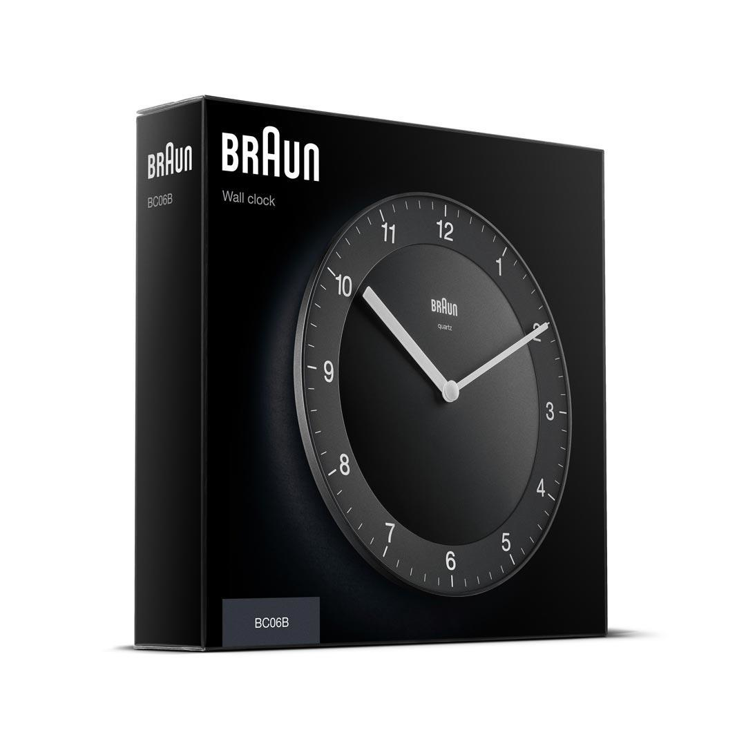 Schwarze Braun Wanduhr in einer schwarzen Box. Das Zifferblatt ist schwarz mit weißen Zeigern und Zahlen. Die Box hat das Braun-Logo.
