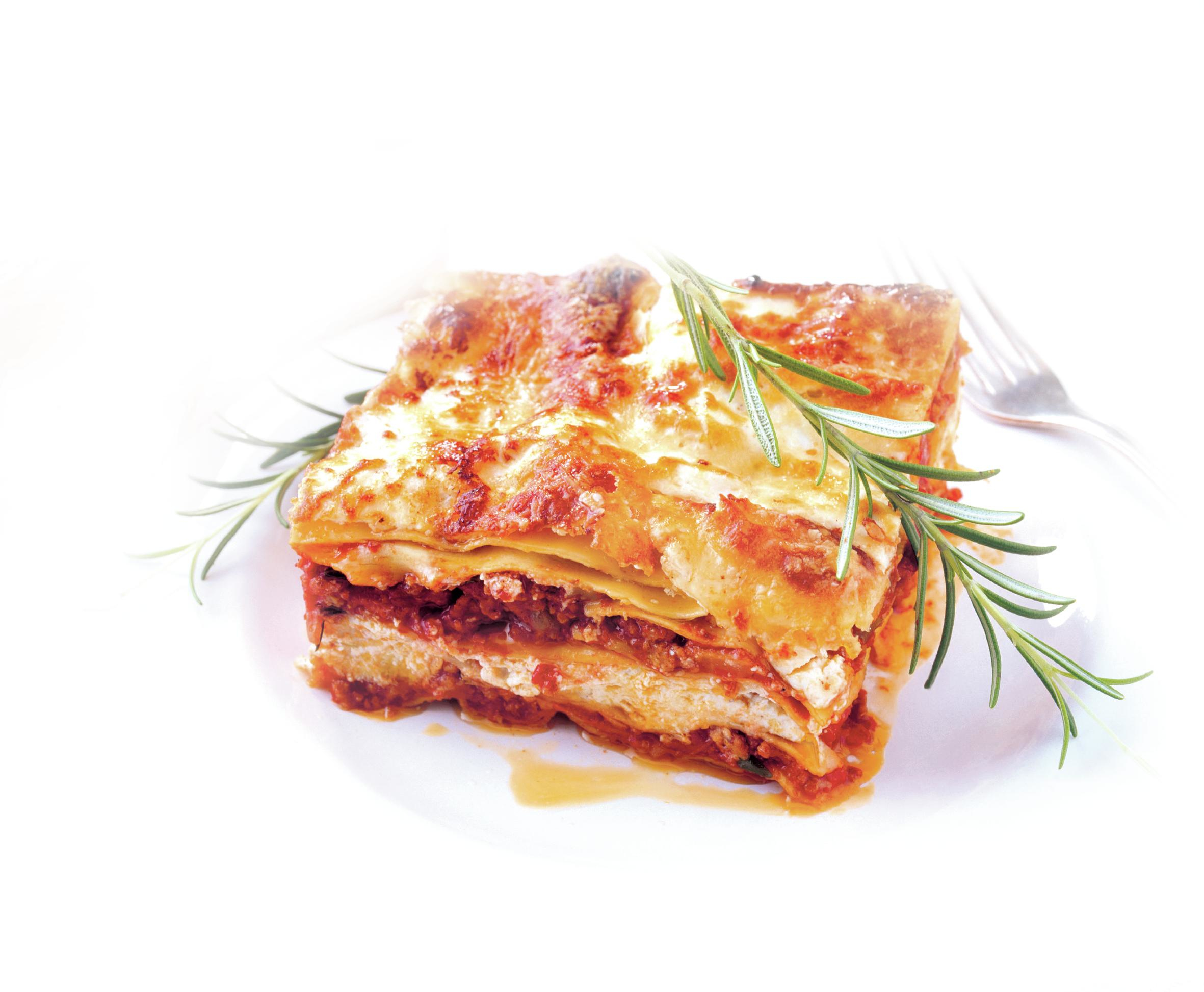 Lasaña en un plato blanco, cubierta con romero. Las capas consisten en pasta, salsa y queso. Un tenedor está en el fondo.